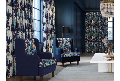 Living room with dark blue walls, patterned curtains, two dark blue armchairs with floral upholstery, a white table, a black floor lamp, and a chandelier.