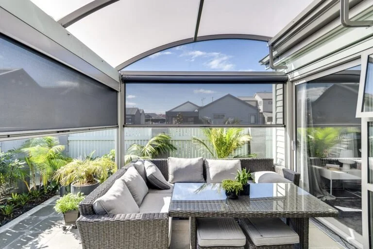 Enclosed patio with outdoor sofa and table, potted plants, and a view of neighboring houses.