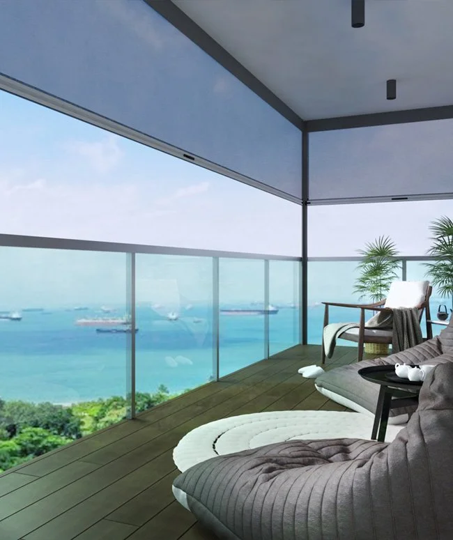 A balcony with glass railing overlooking a body of water with ships. The balcony has wooden flooring, a lounge chair, a small side table, and potted plants.