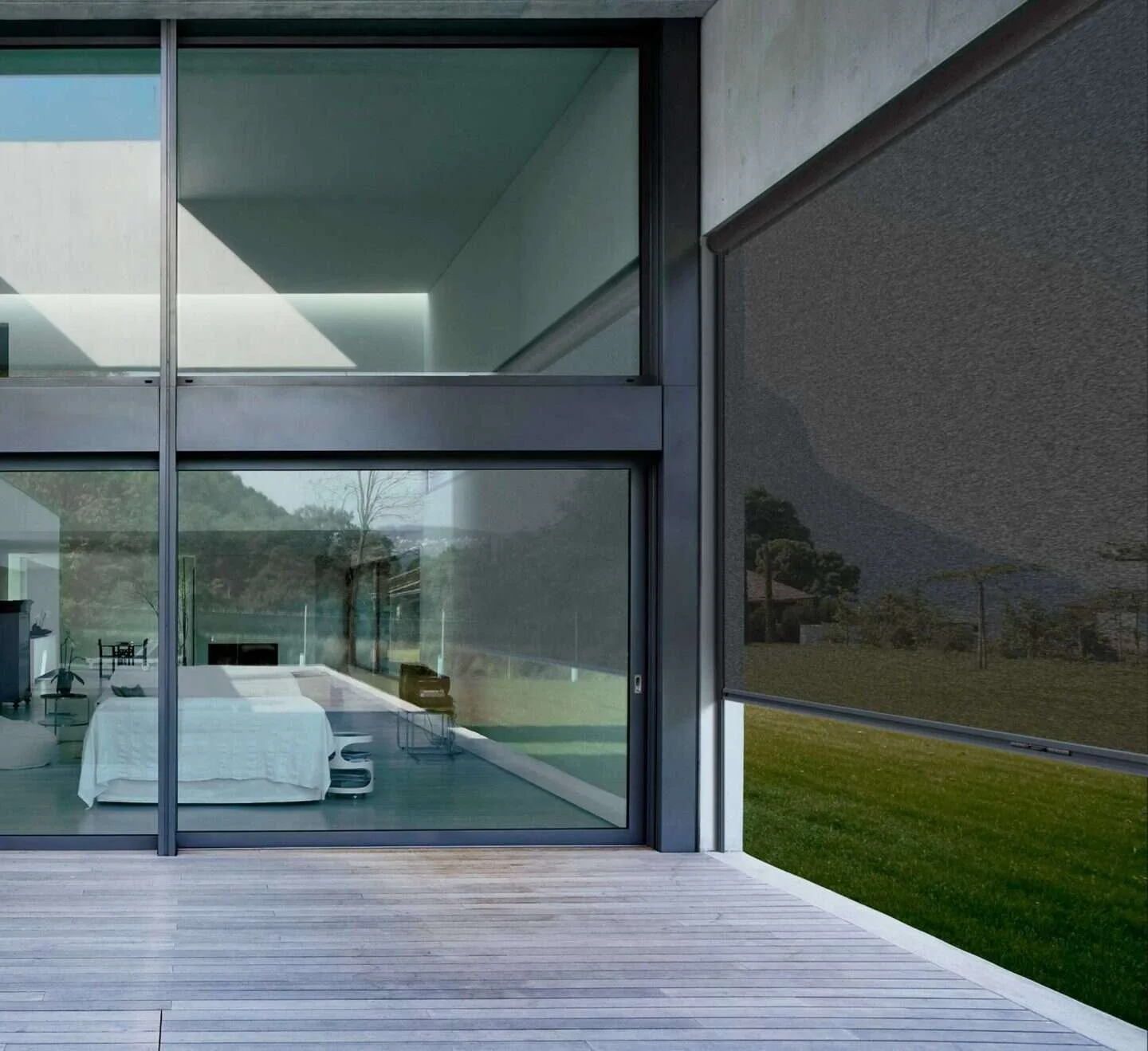Modern house with large glass windows reflecting outdoor landscape, including grass and trees, and interior with minimalistic bedroom