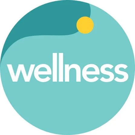 A circular logo with a turquoise background, featuring the word "wellness" in white lowercase letters, a small yellow circle, and a dark teal shape.