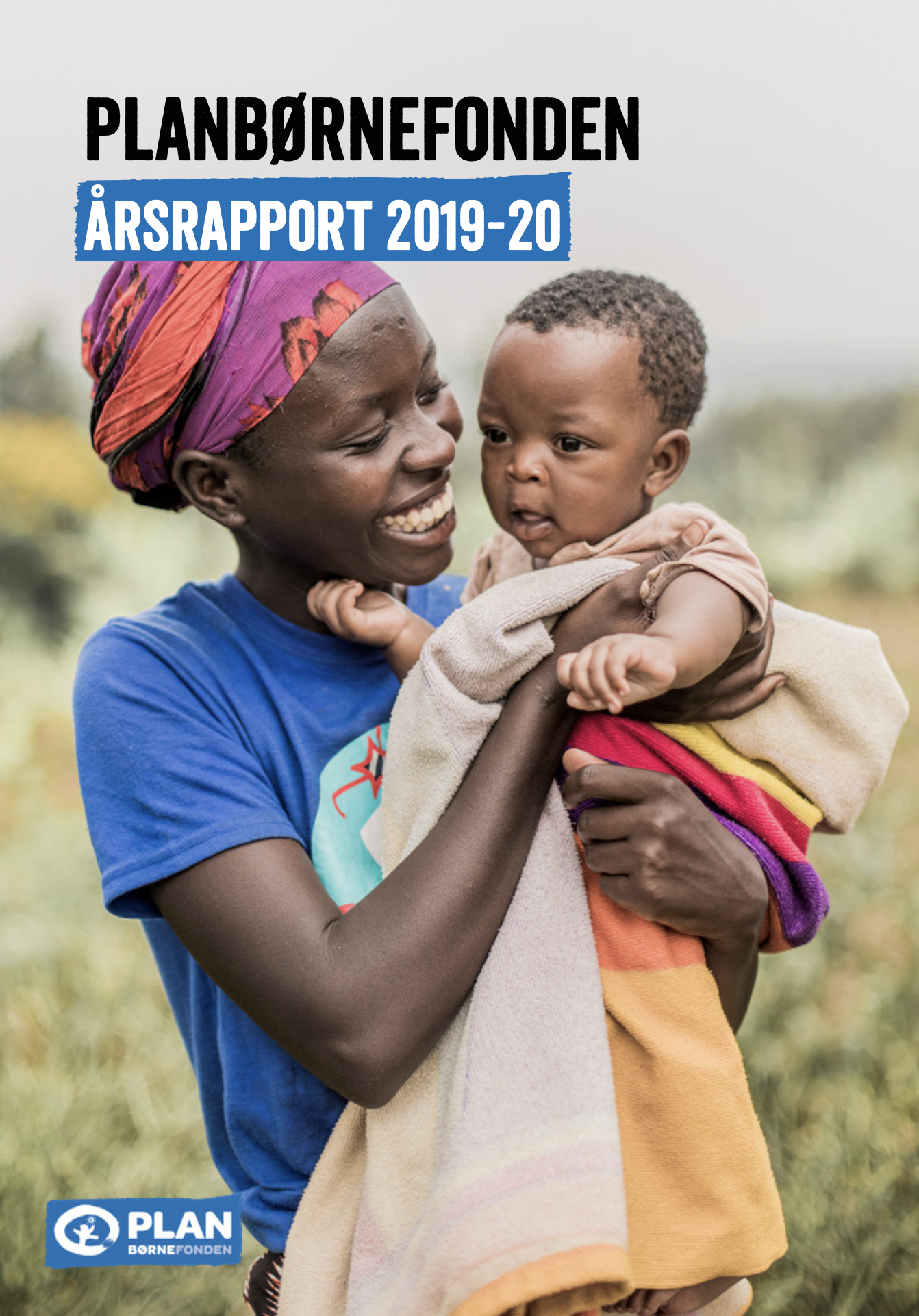 En kvinde med farvet hovedtørklæde holder en baby i sine arme. Kvinden smiler, og babyen ser på med åben mund i et udendørs miljø.