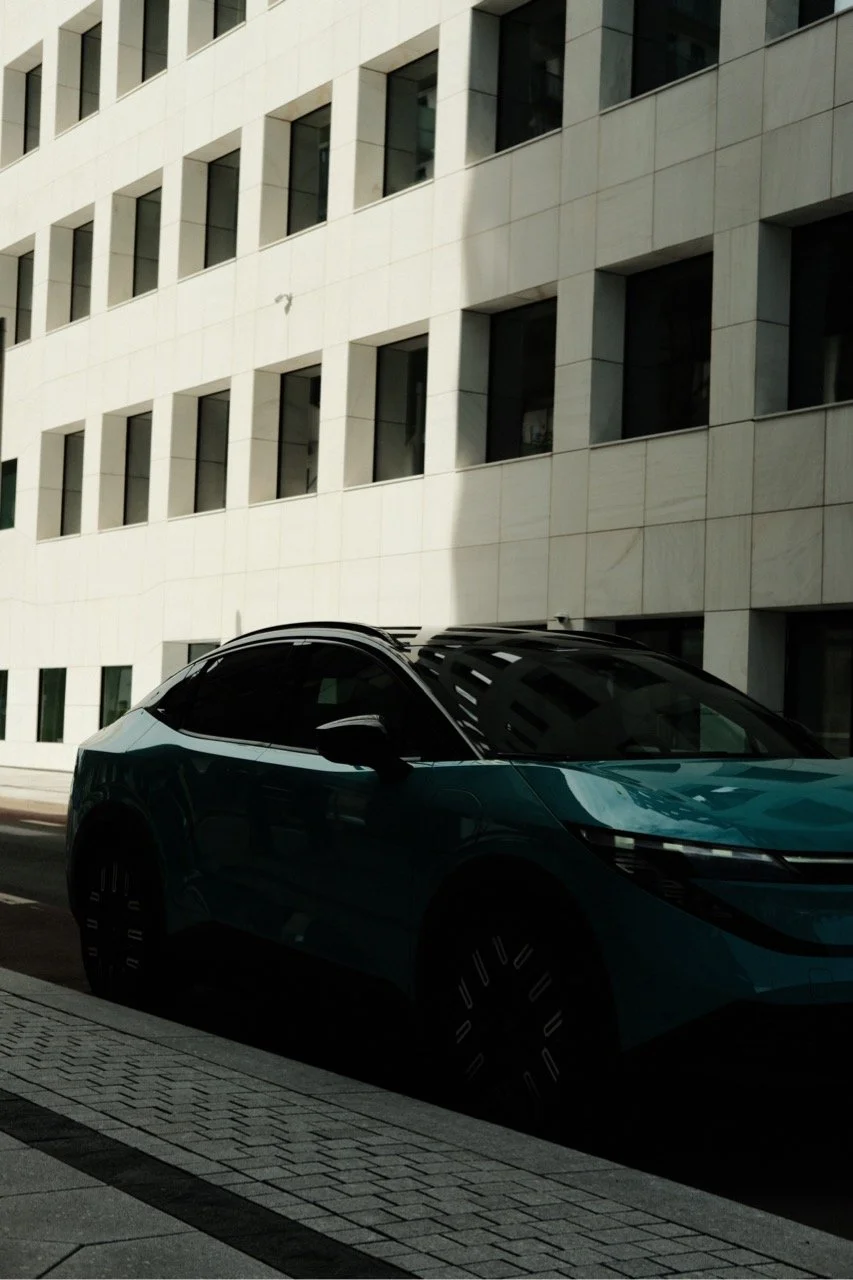 Behind the scene look at a film production in Norway. Monky Productions Production Service Norway. A modern teal-colored electric car parked on a city street near a white building with square windows.