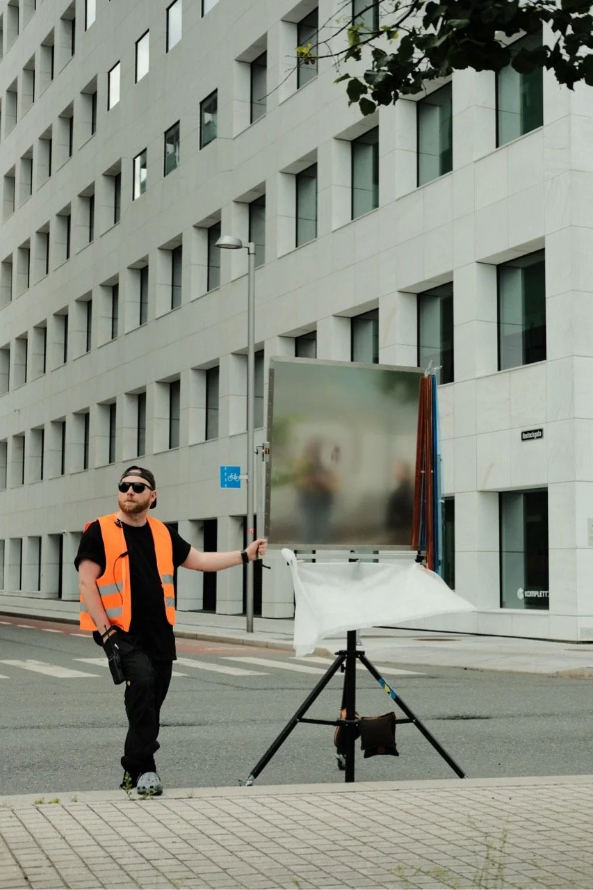 Behind the scene look at a film production in Norway. Monky Productions Production Service Norway. A man wearing sunglasses and an orange safety vest standing next to an easel on a city street.