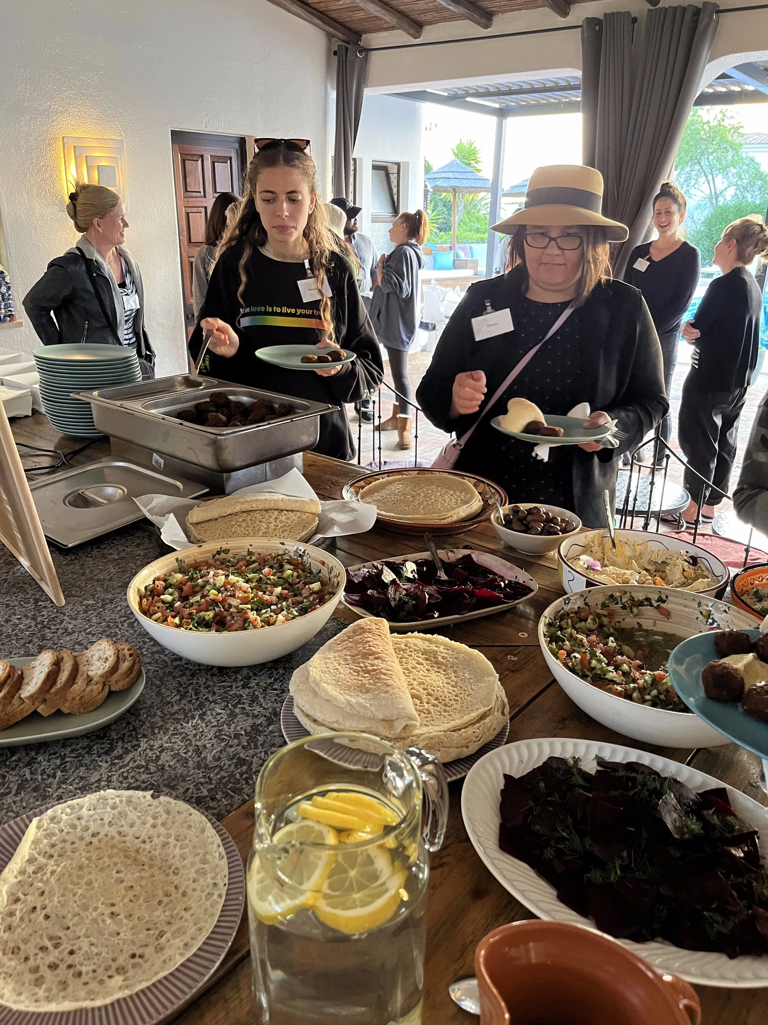 People serving themselves food at a buffet with salads, bread, and various dishes at an indoor event.