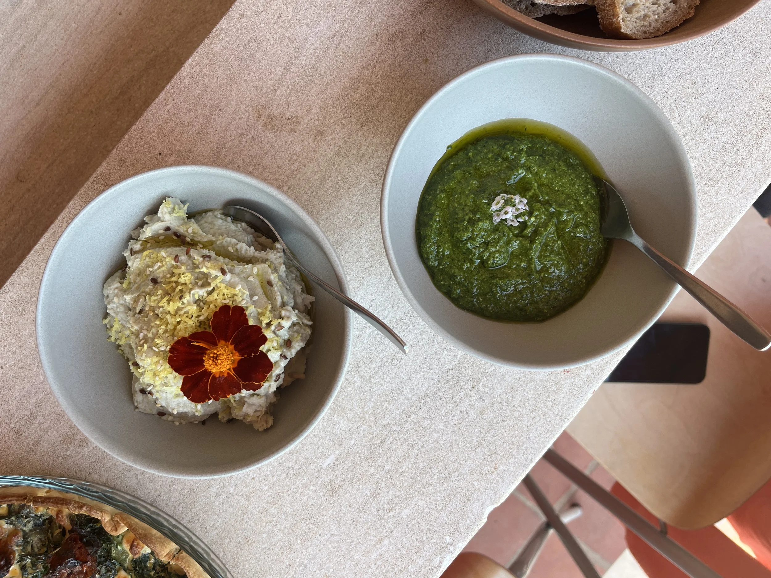 Two bowls on a table, one with a green spinach or herb-based dish and the other with a creamy salad garnished with a red flower