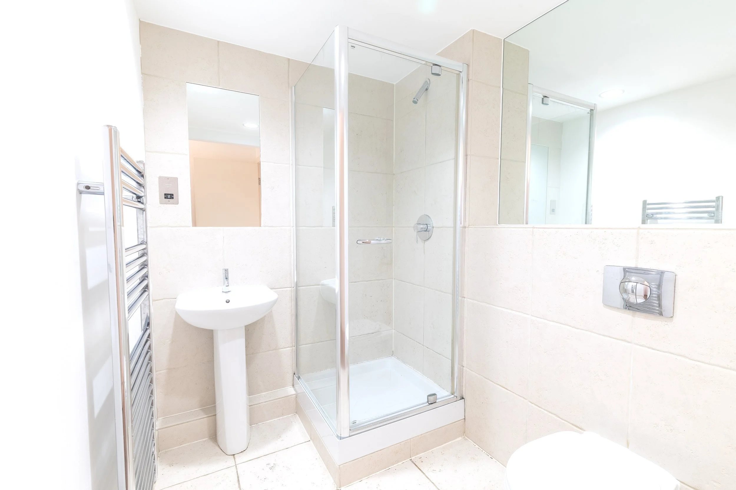 Modern bathroom with a glass shower enclosure, wall-mounted sink, tiled walls, and a heated towel rack.