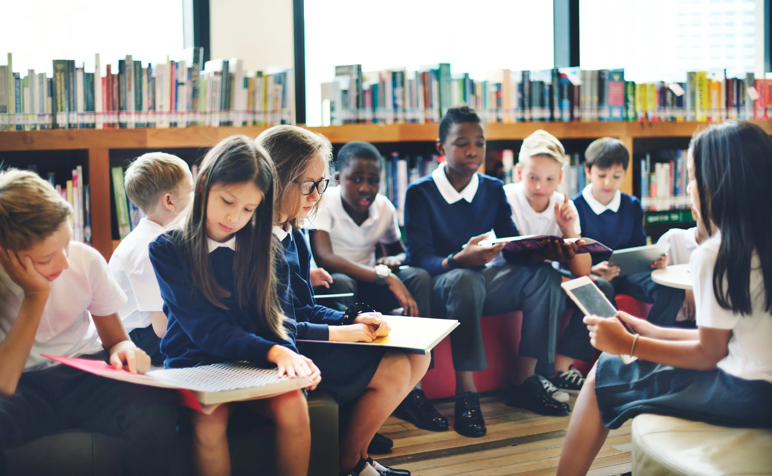 A diverse group of school children reading and using electronic devices in a library