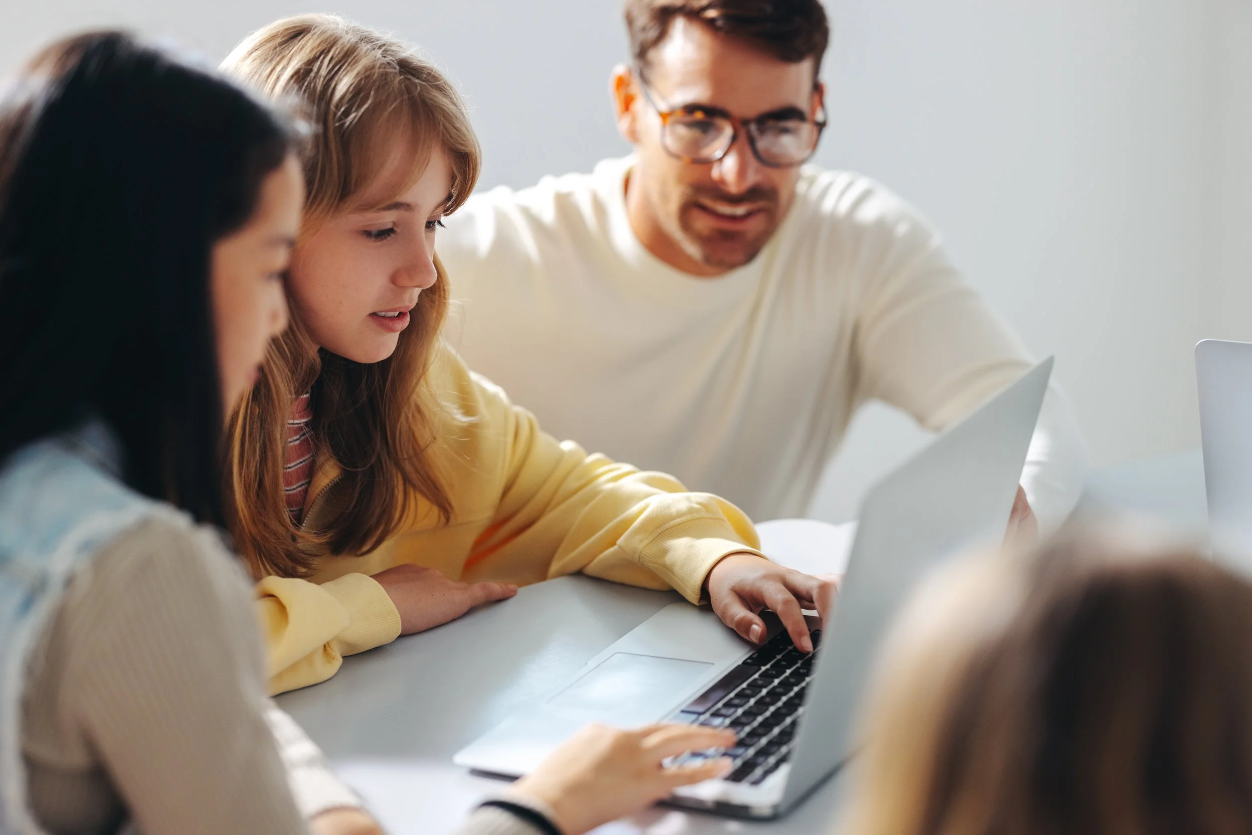 A group of young students with their teacher working on a laptop in a classroom.