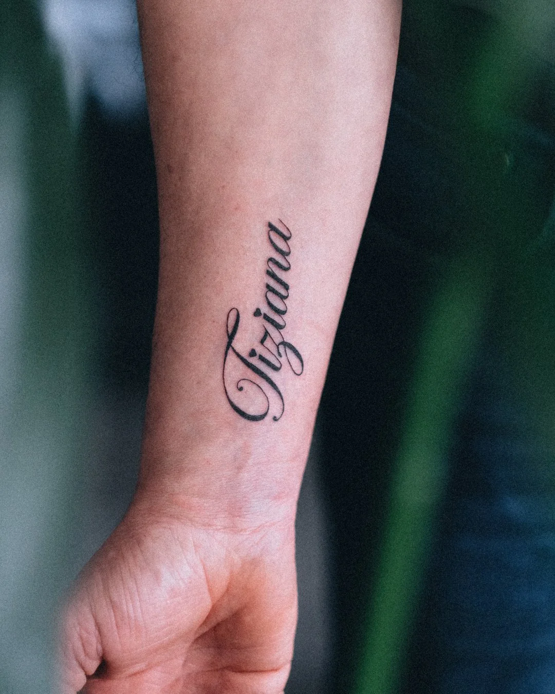 Fine line script tattoo of the name Tiziana on the forearm by Leandro Correia in Zurich