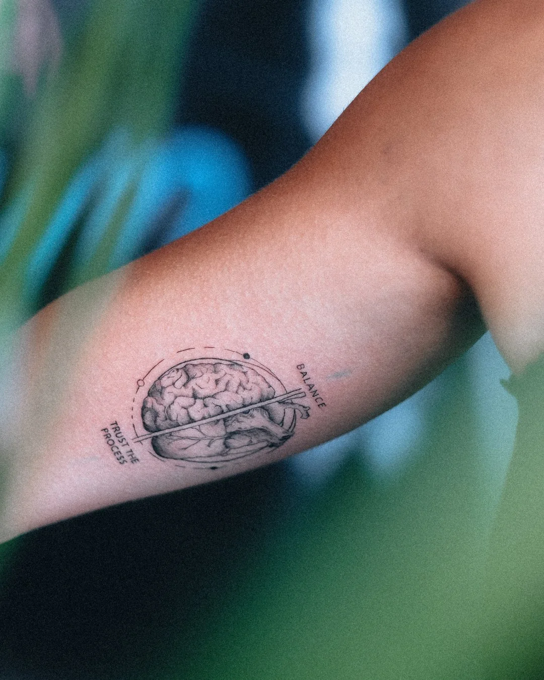 Fine line brain tattoo with circular design and lettering on the inner arm by Leandro Correia in Zurich