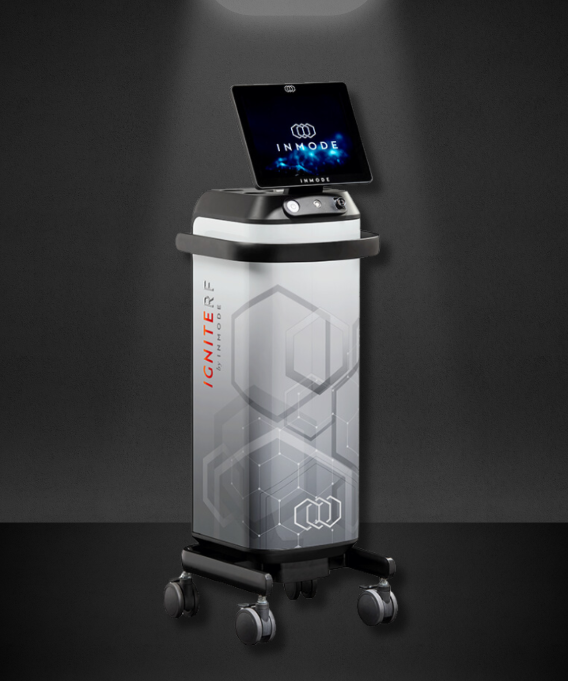 Medical device with a display screen on top and branding for IGNITE by INMODE, placed against a black wall.