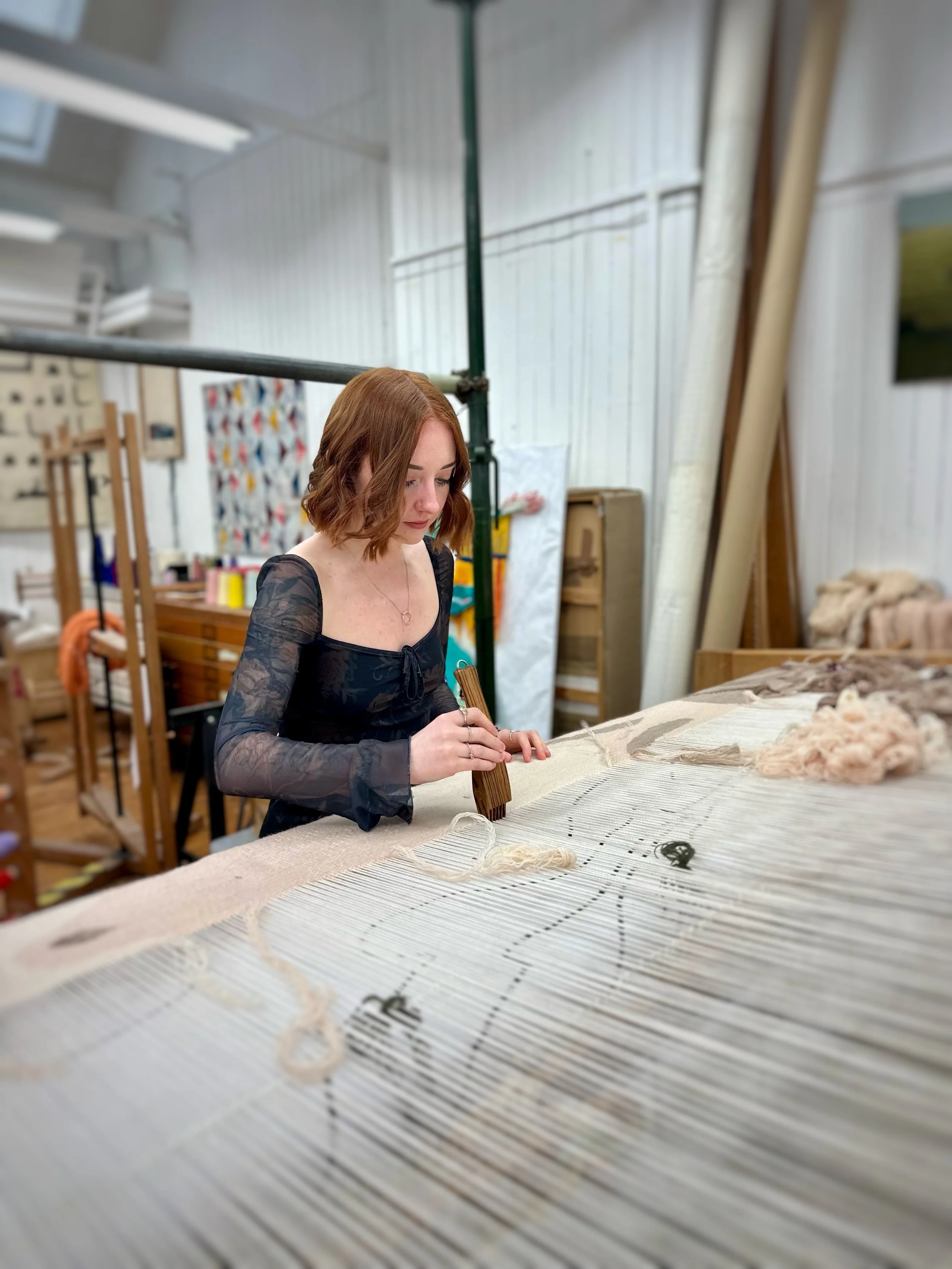 The image is a photograph of the artist weaving at the loom