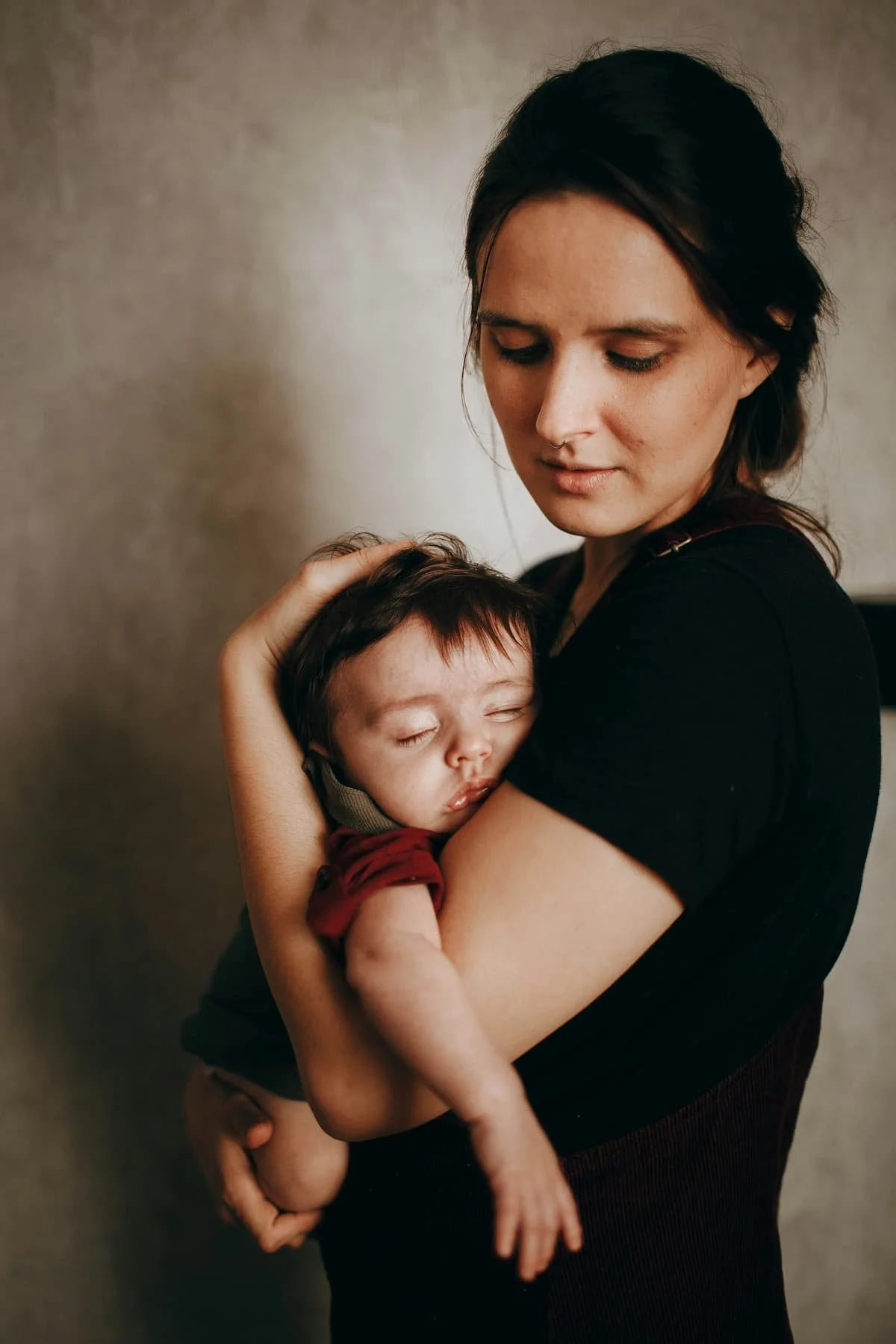 Mother holding sleeping newborn with distant expression during postpartum depression therapy in Miami FL