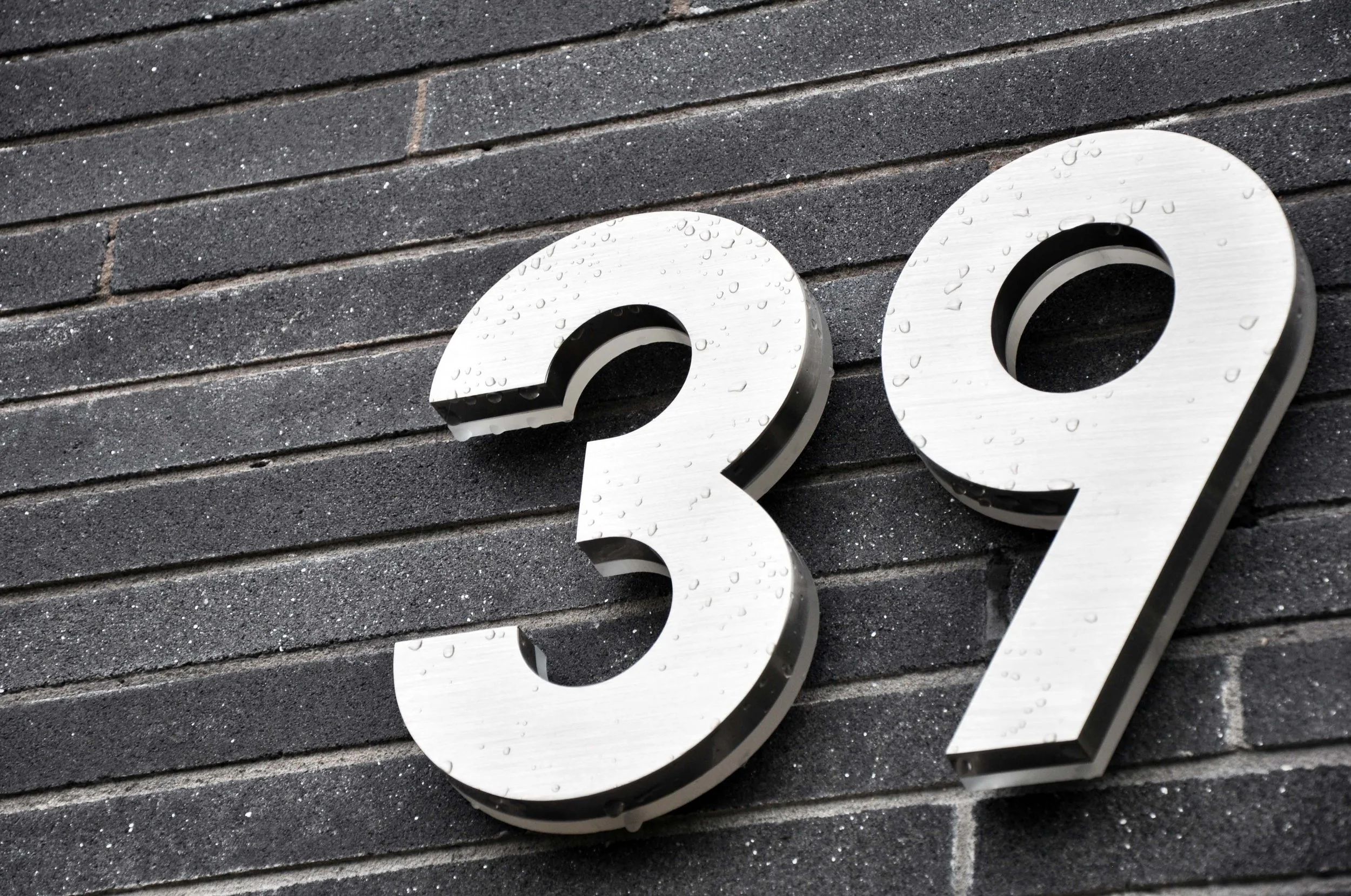 Unity Architects — Close-up architectural detail of metal house numbers on grey brickwork for a bespoke residential project in Warwickshire.