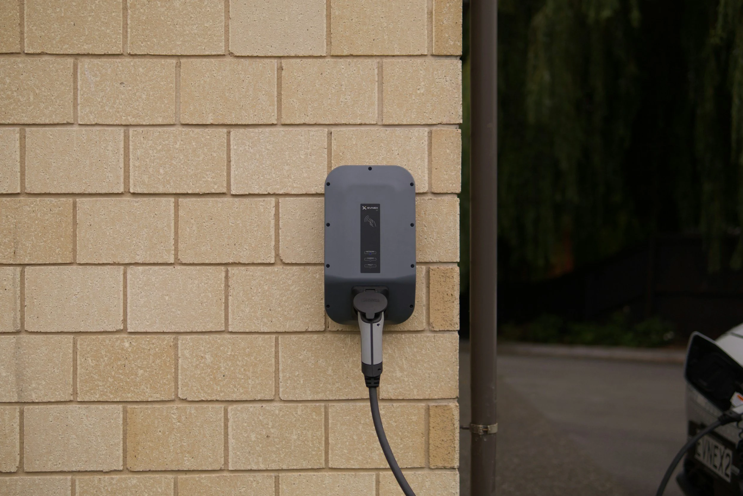 Electric vehicle charging station mounted on a beige brick wall, with a charging cable attached.