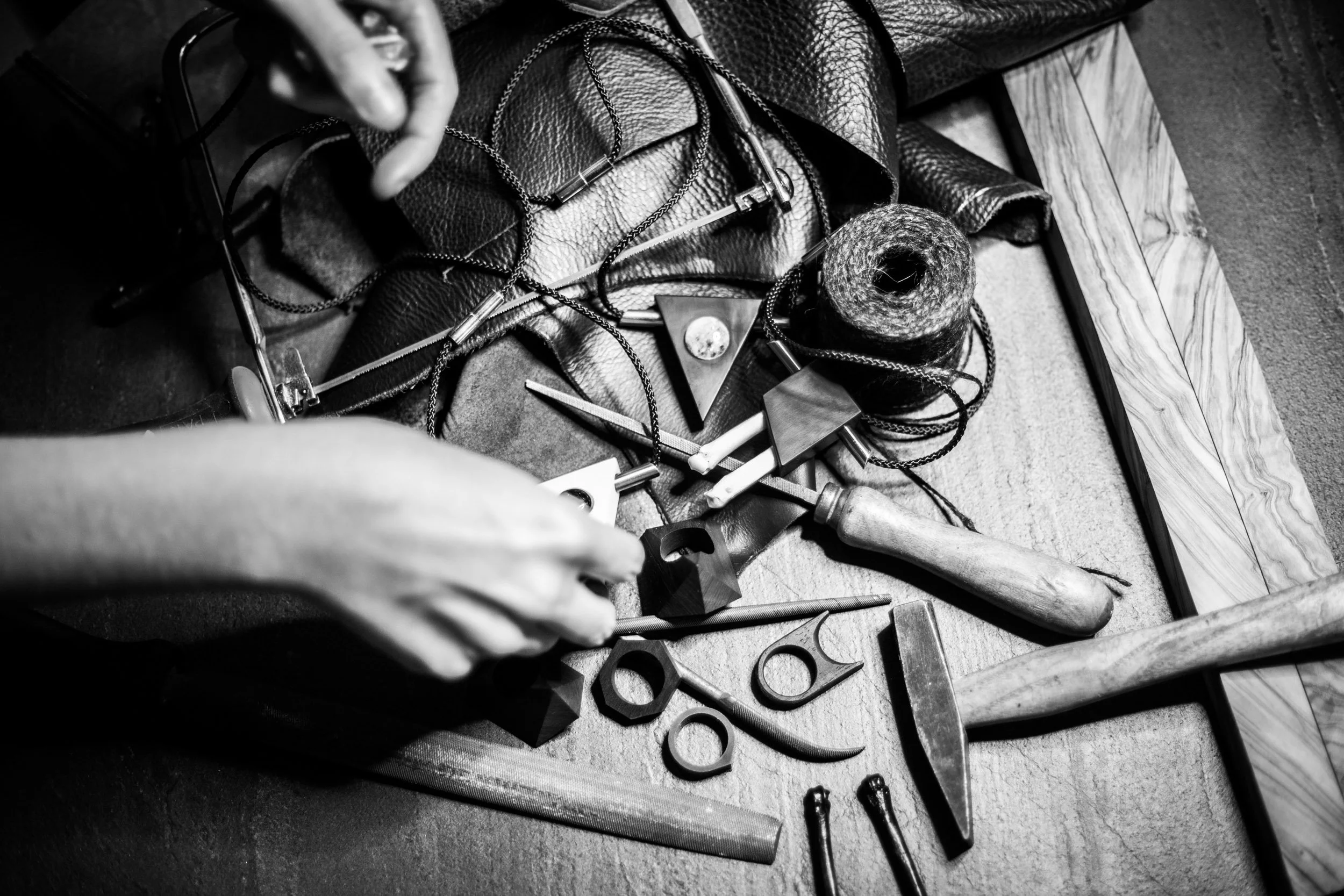ISAROS workbench, hands at work among files, hammers and finished pieces, black and white image
