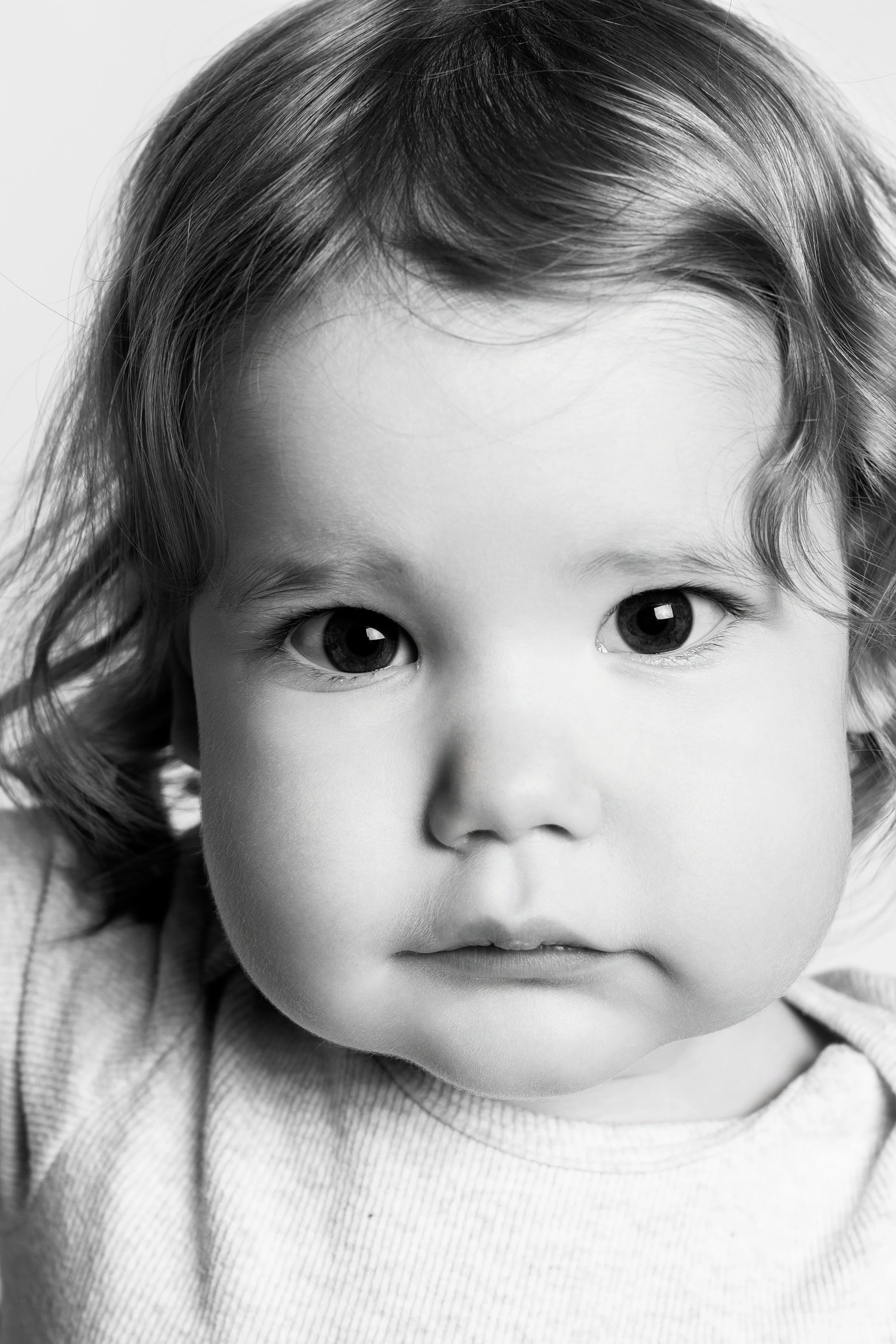 Black and white close-up portrait of a young child with wavy hair, big eyes, and a neutral expression.