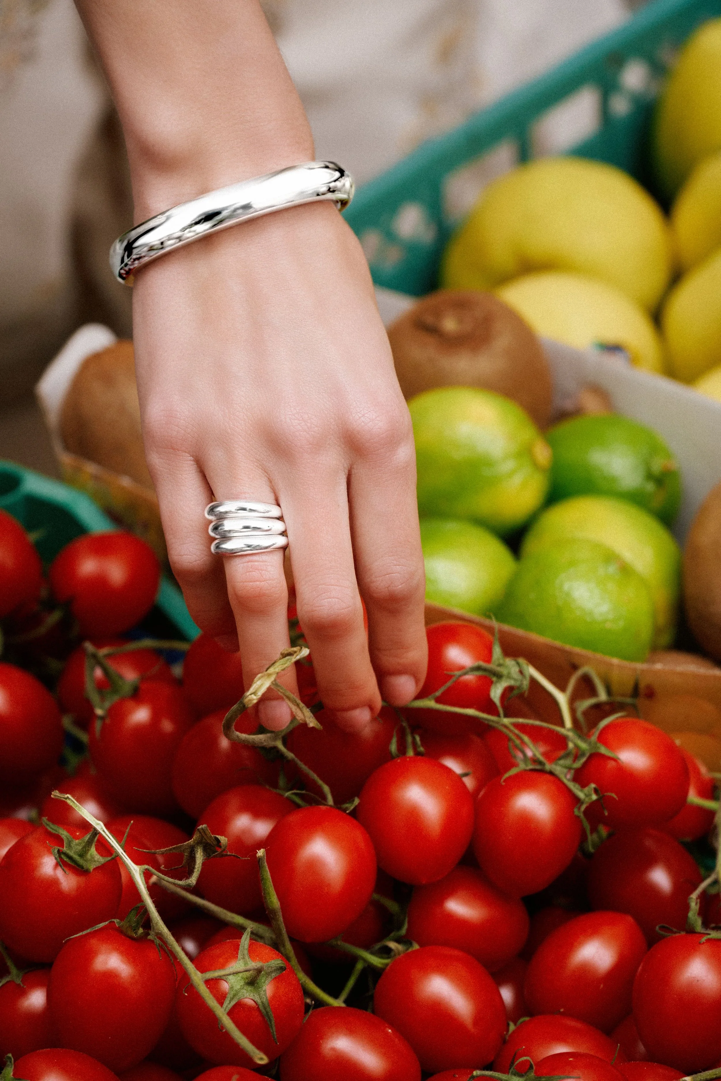 hand with silver bracelet and ring selecting a tomato.