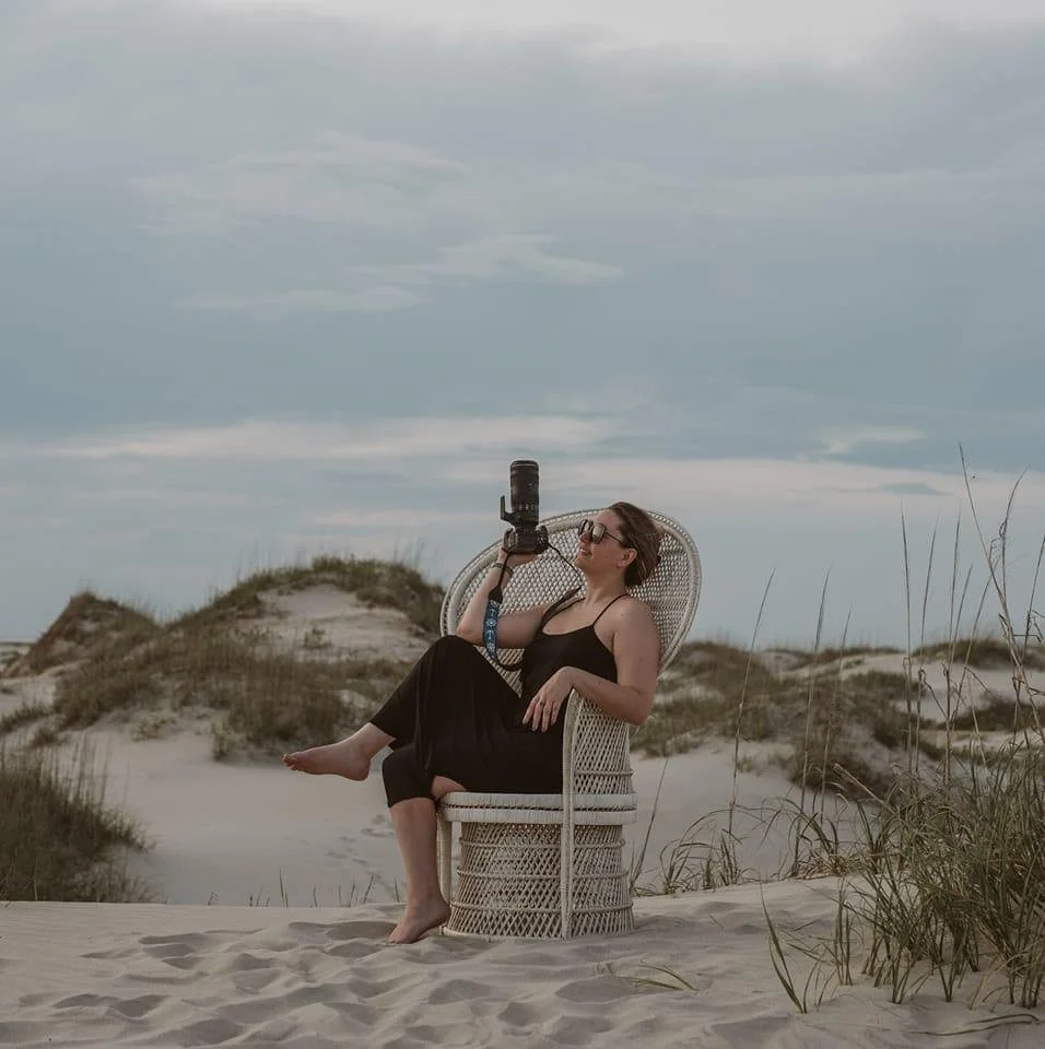 girl sitting in a chair on the beach holding a camera