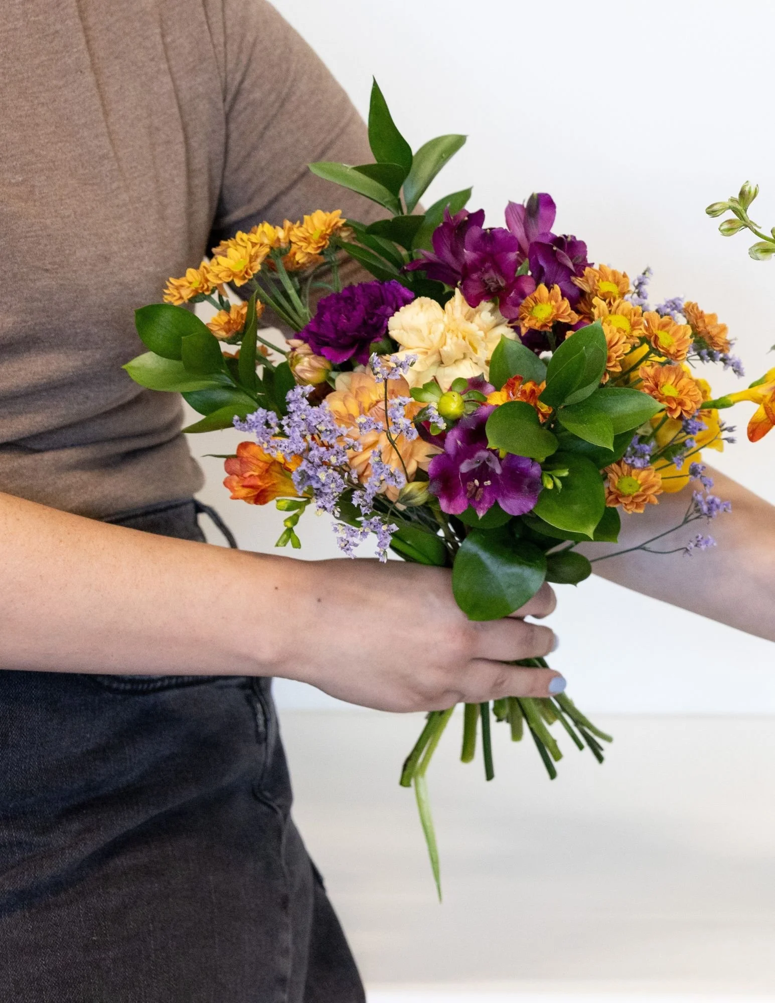 Person holding a colorful bouquet of various flowers including roses, daisies, and greenery.