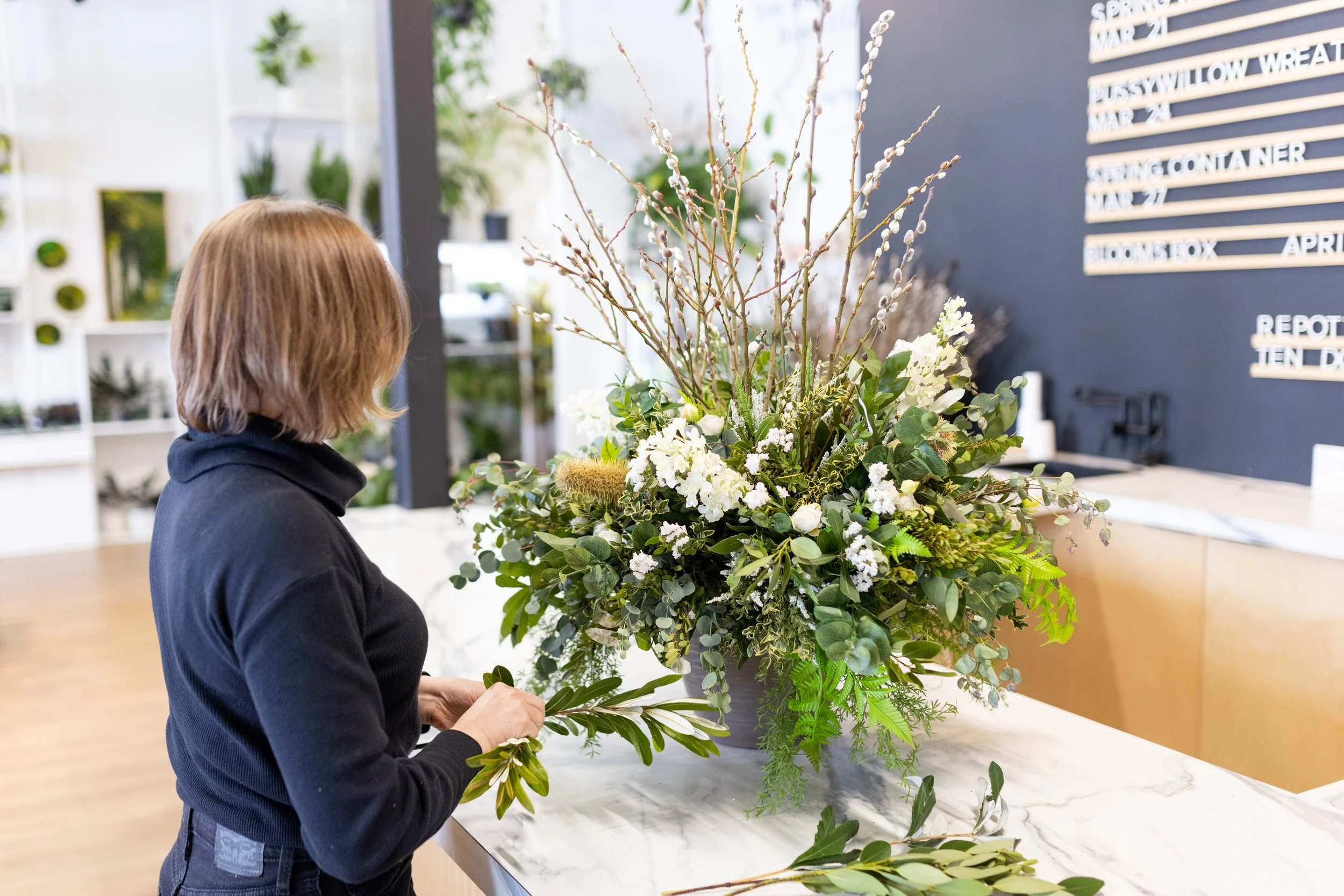 Spring container arrangement being designed in Bloom Culture’s Calgary studio with fresh greens, pussy willow, and seasonal branches.