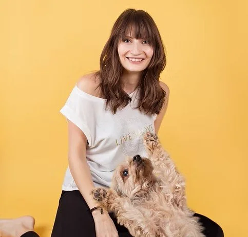 Young woman smiling with a dog against a yellow background.