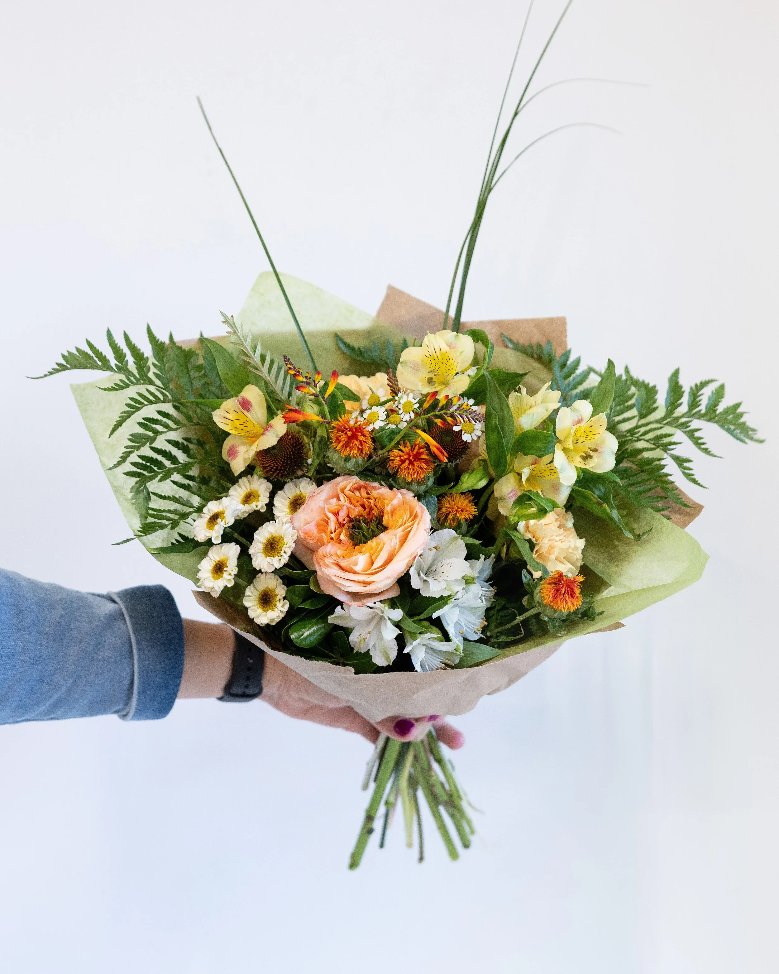 Person holding a colorful bouquet of flowers including daisies, tulips, and carnations.