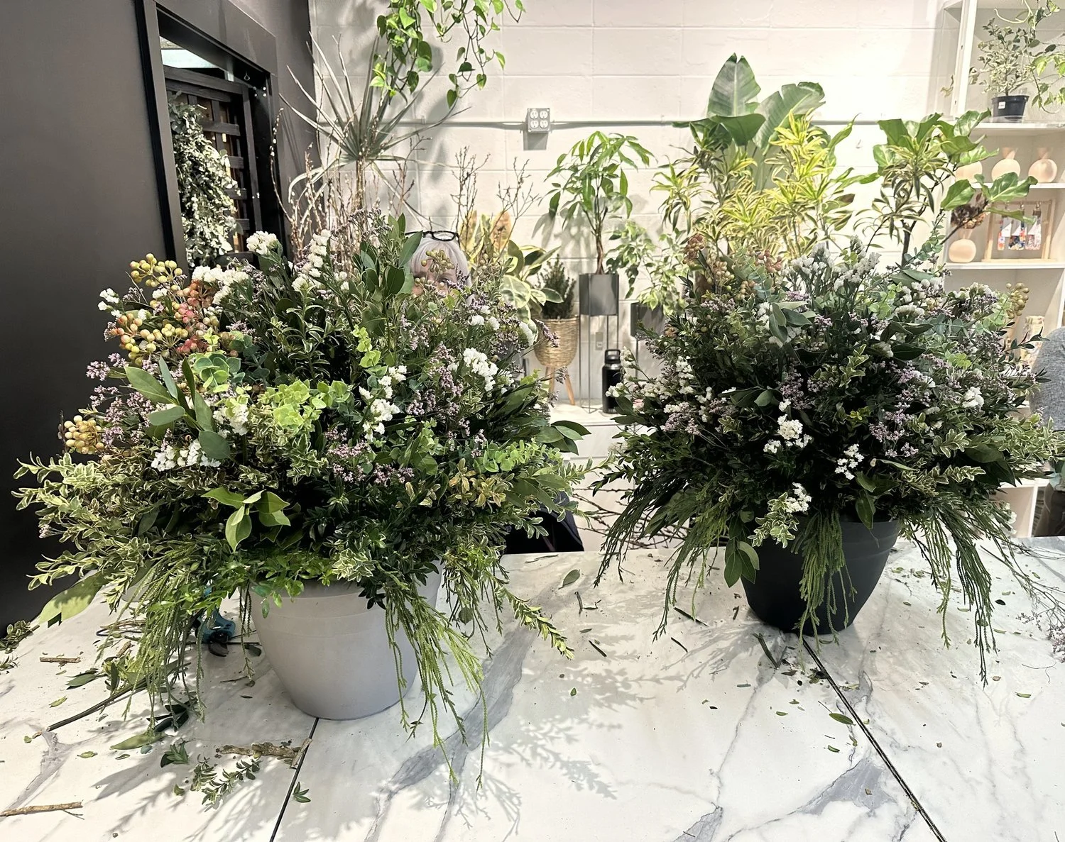 Two handcrafted spring outdoor planter featuring a mix of fresh greens, dried flowers, and decorative elements.