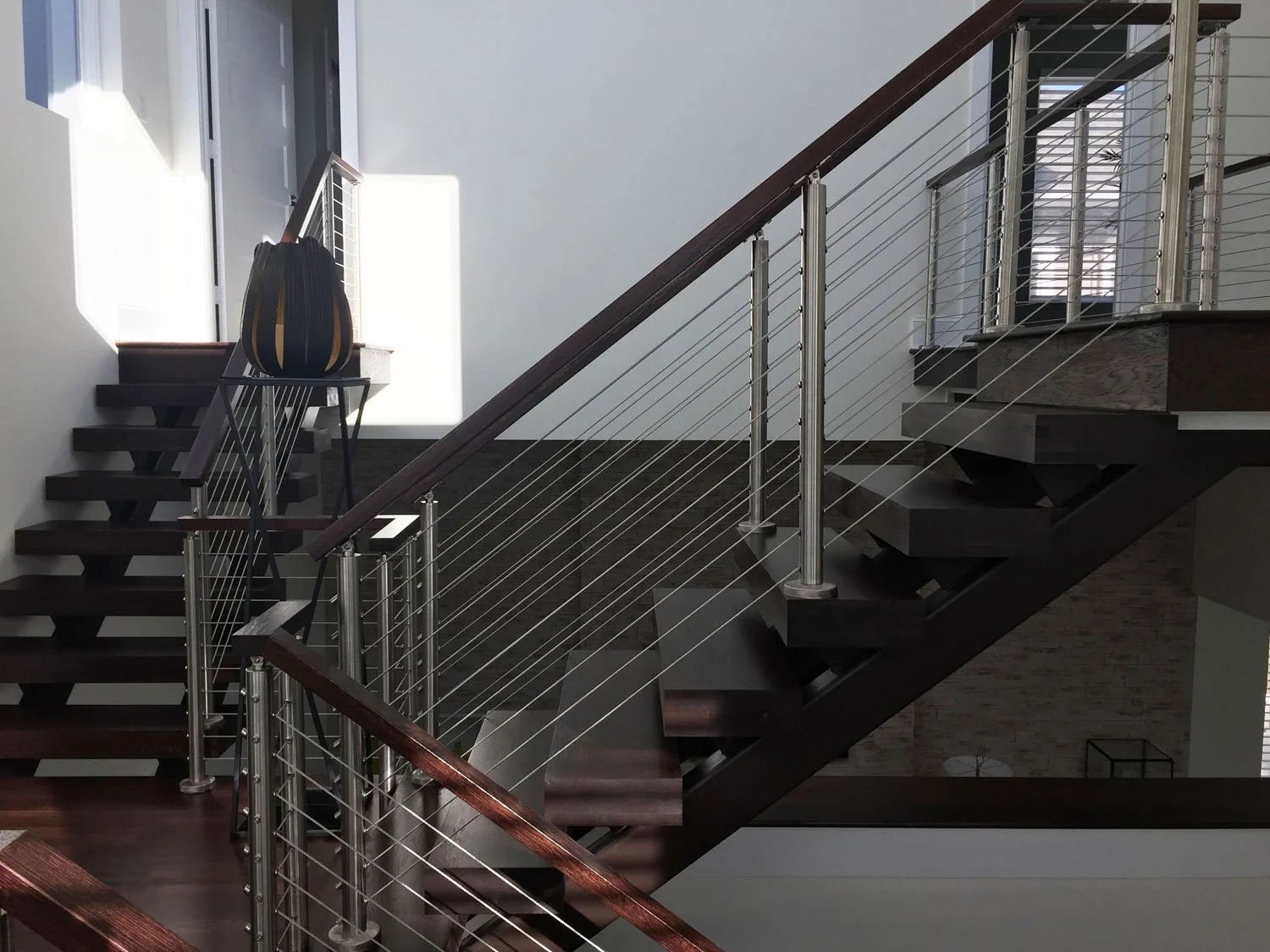 Modern staircase with dark wooden steps, metal railing, and glass panel balustrades inside a well-lit house.