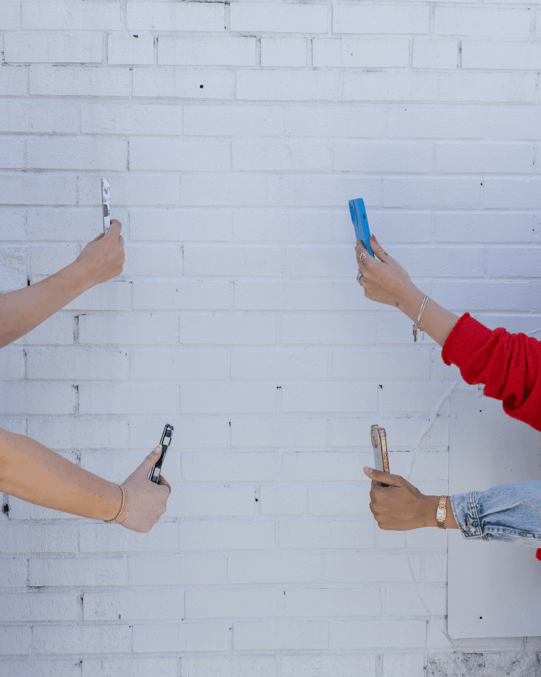 Four people holding smartphones against a white brick wall, representing the Cucamonga Media social media team.