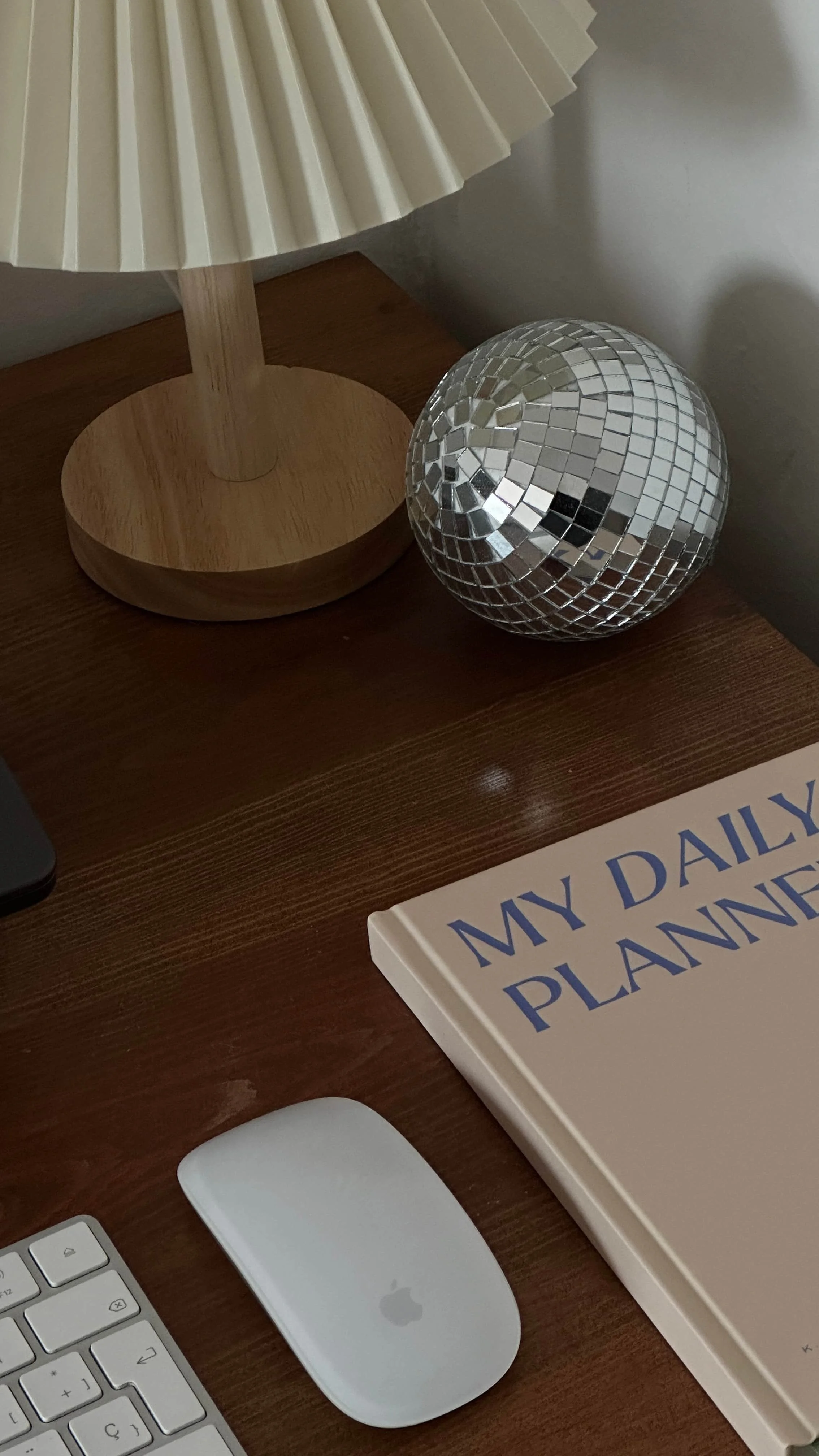 A styled desk setup with an Apple keyboard and mouse, a daily planner, a mini disco ball, and a pleated lamp — fractional marketing agency workspace.