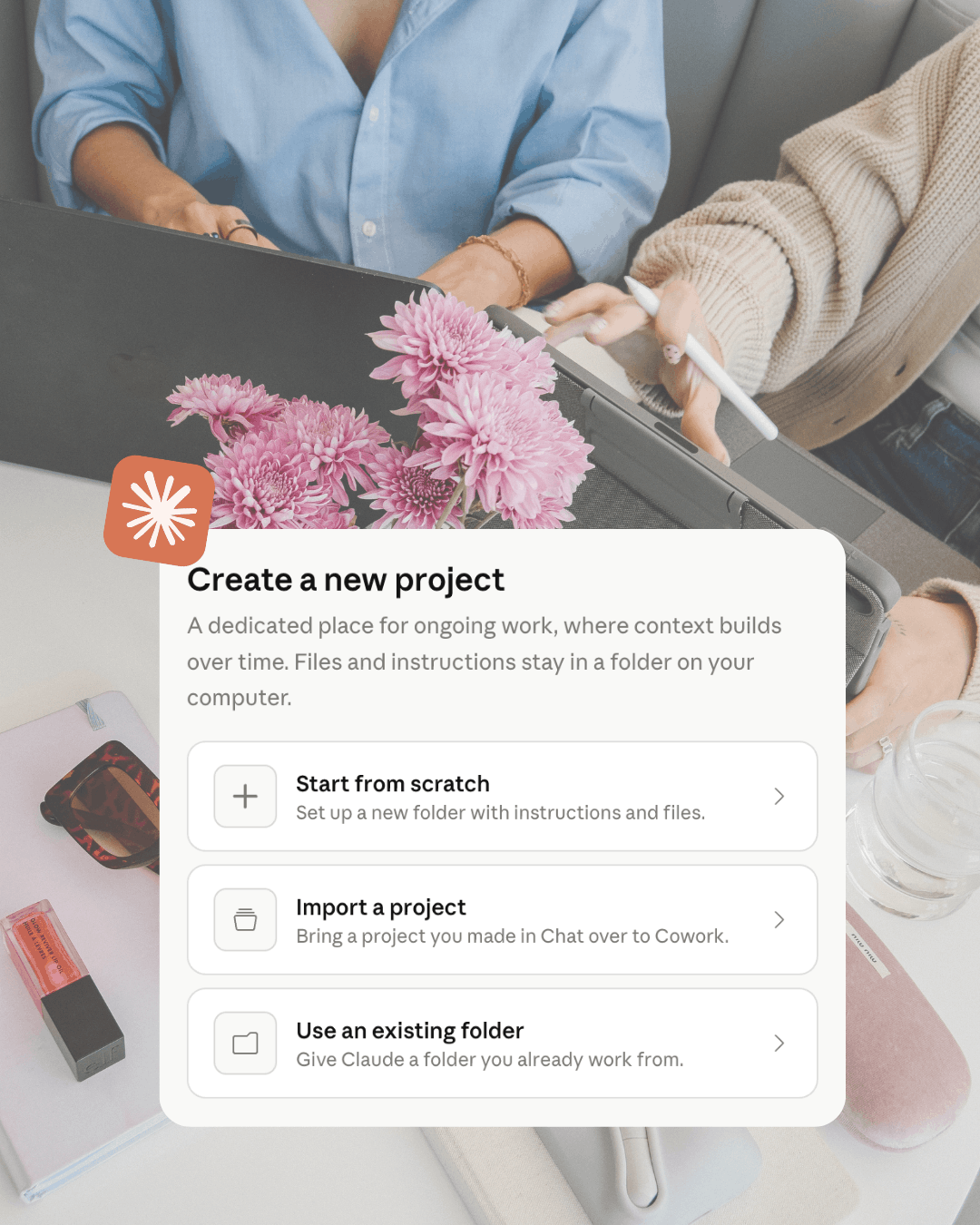 Screenshot of Cowork's 'Create a new project' menu with options to start from scratch, import a project, or use an existing folder, overlaid on a photo of two people at a desk with a laptop, tablet, and pink flowers.