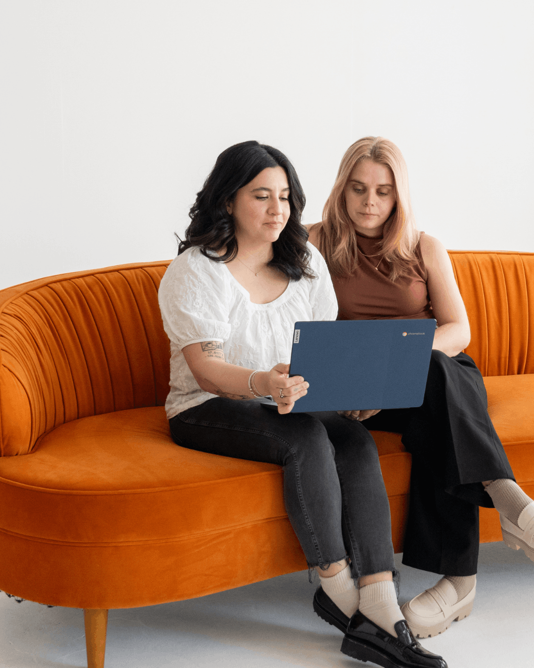 Alix, owner of Cucamonga Media, and a team member sitting together on an orange couch reviewing a laptop, representing the people behind the brand's community-first approach