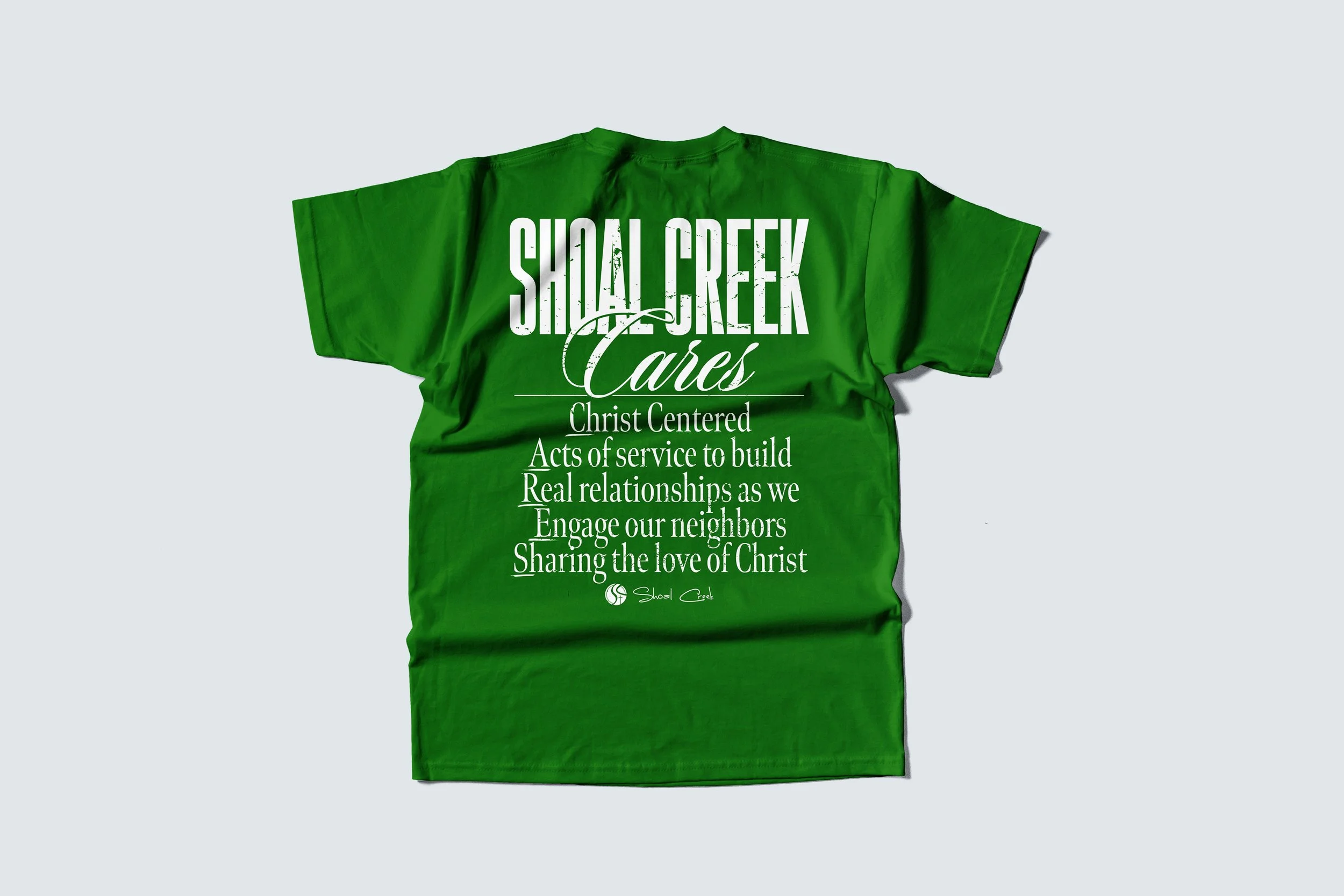 Green T-shirt with white text promoting Shoal Creek Cares, highlighting acts of service and love of Christ.