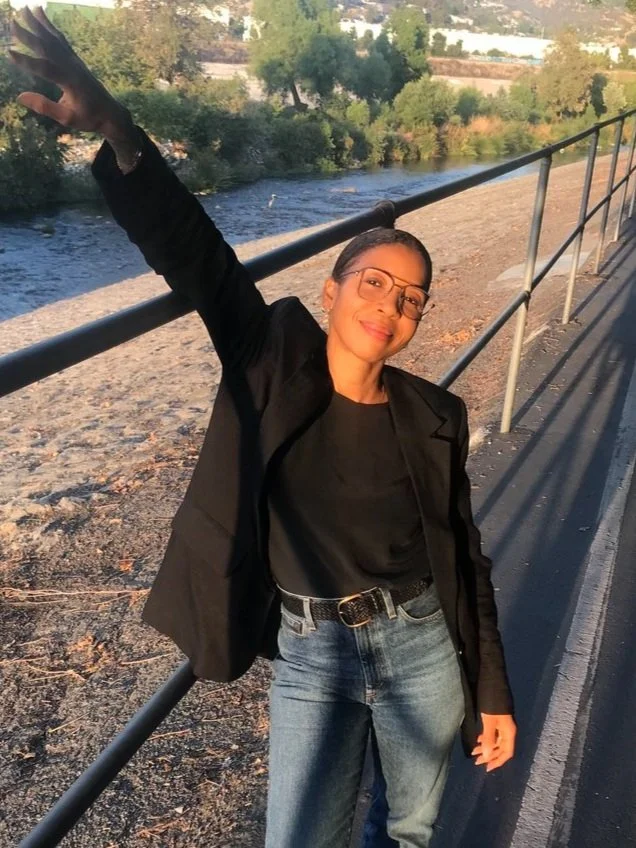 Dana smiles at camera, wearing glasses and a black shirt and jacket, happy about her website.