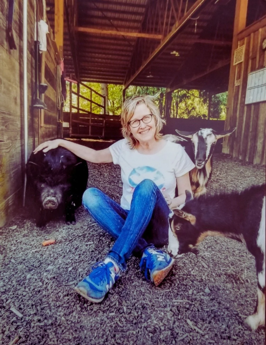 Lori sits on the ground in a barn with goats