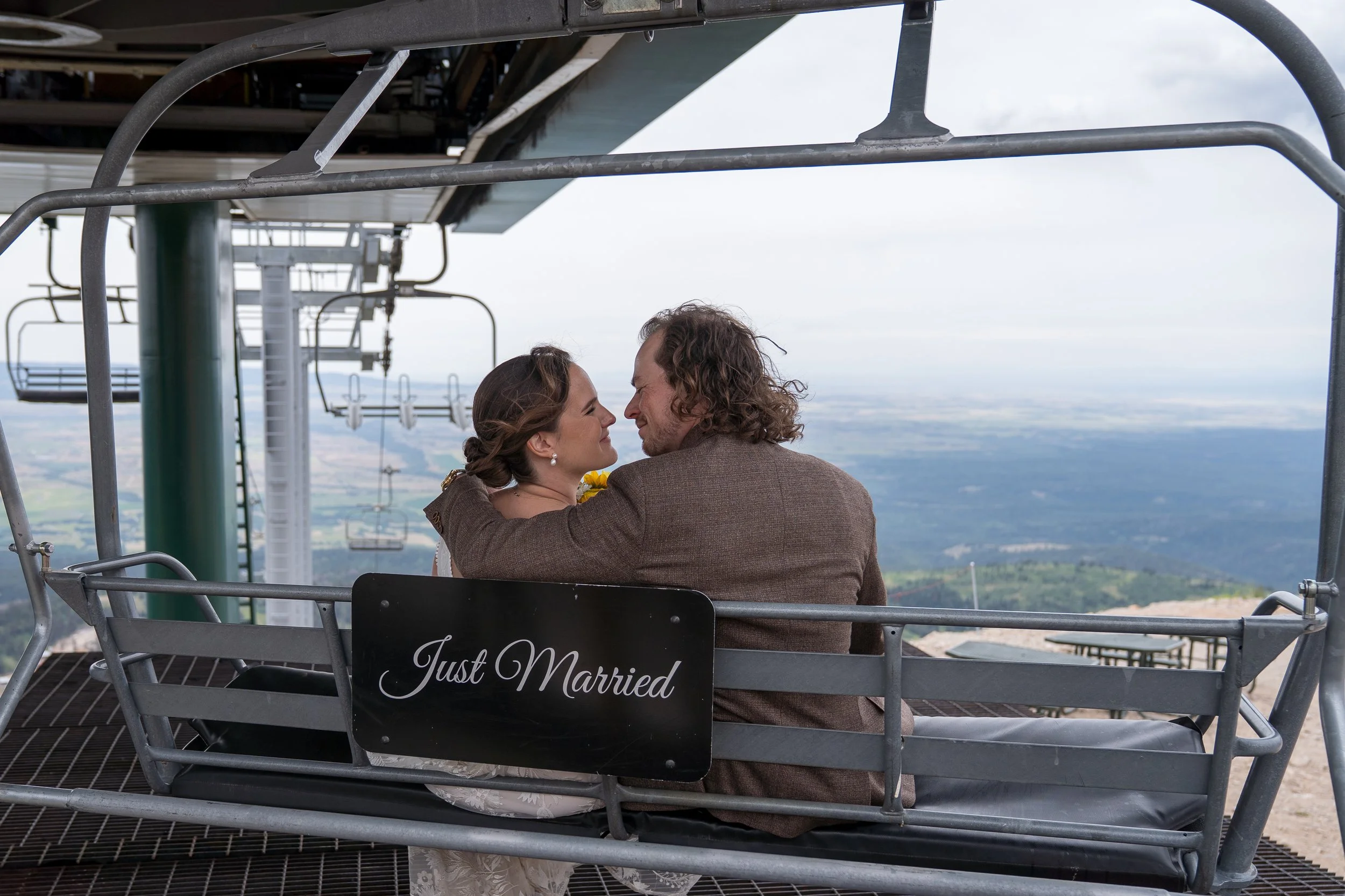 Grand Targhee Resort, documentary Wedding photography; bride and groom sit on ski lift with Just Married sign on the back of the chair lift