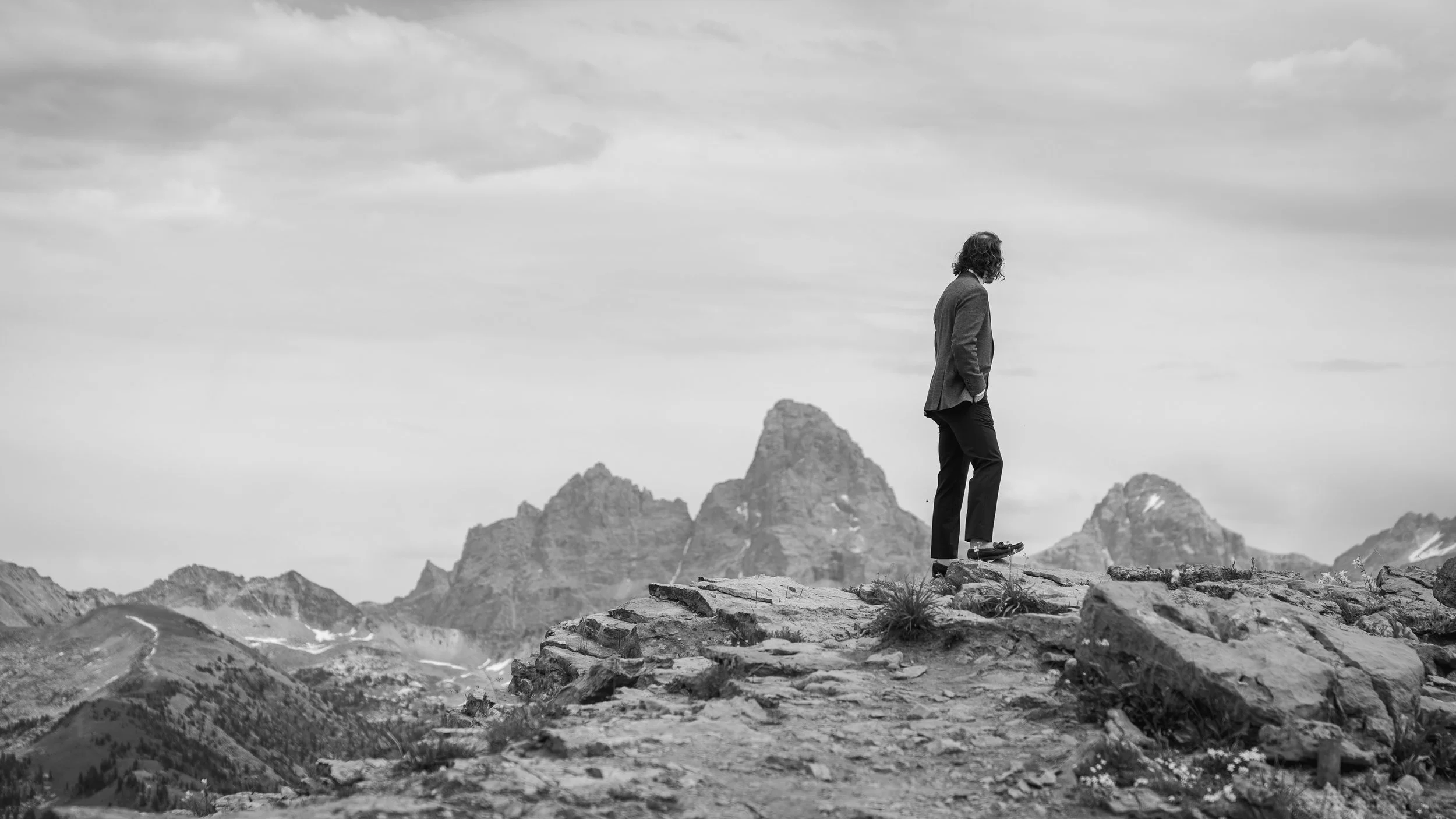 Grand Targhee Resort, documentary Wedding photography; groom stands along ridge overlooking the back side of the Teton Mountain Range