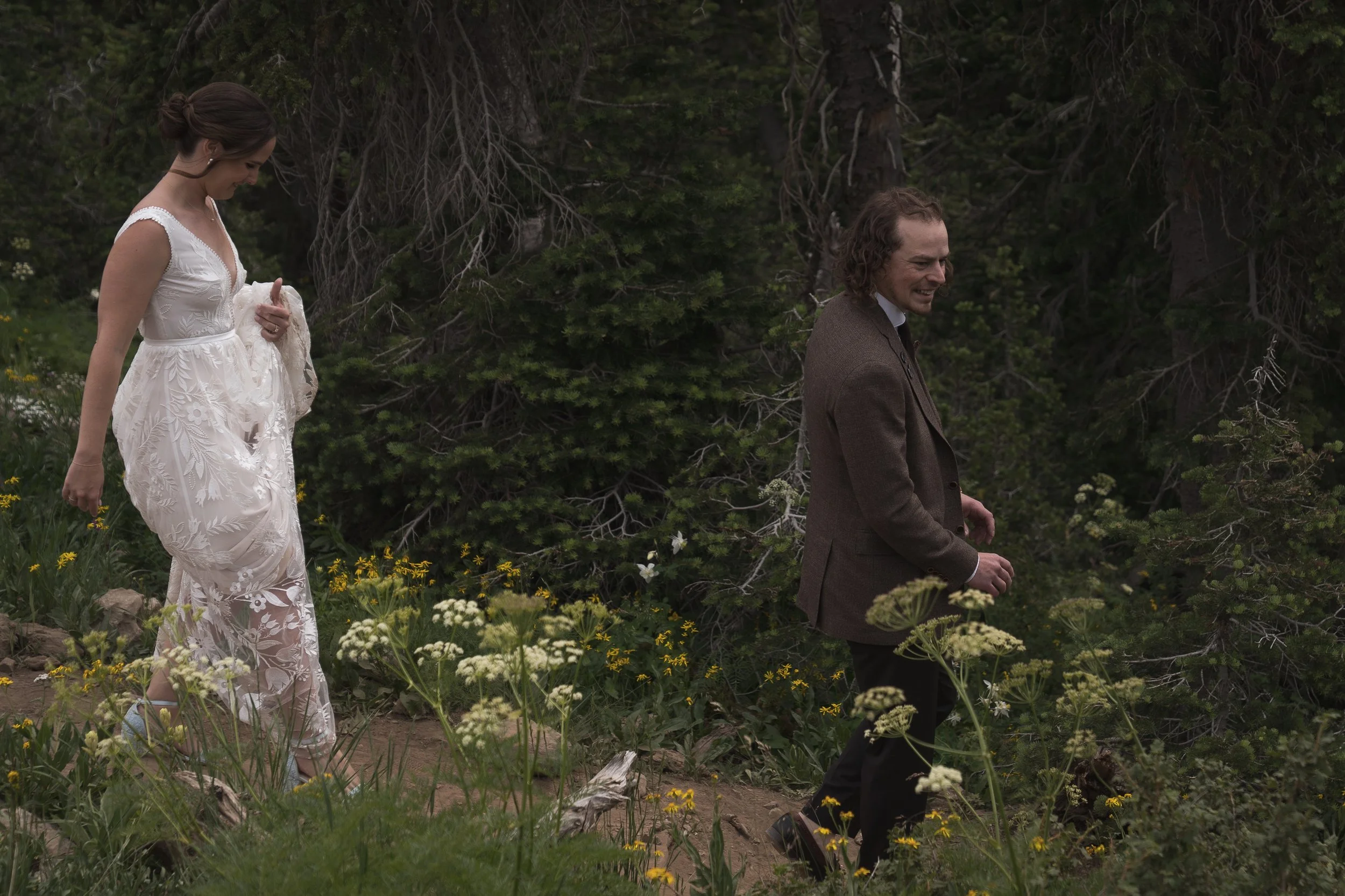 Grand Targhee Resort, documentary Wedding photography; bride and groom walking along a mountain trail with wildflowers in the foreground, pines in the background