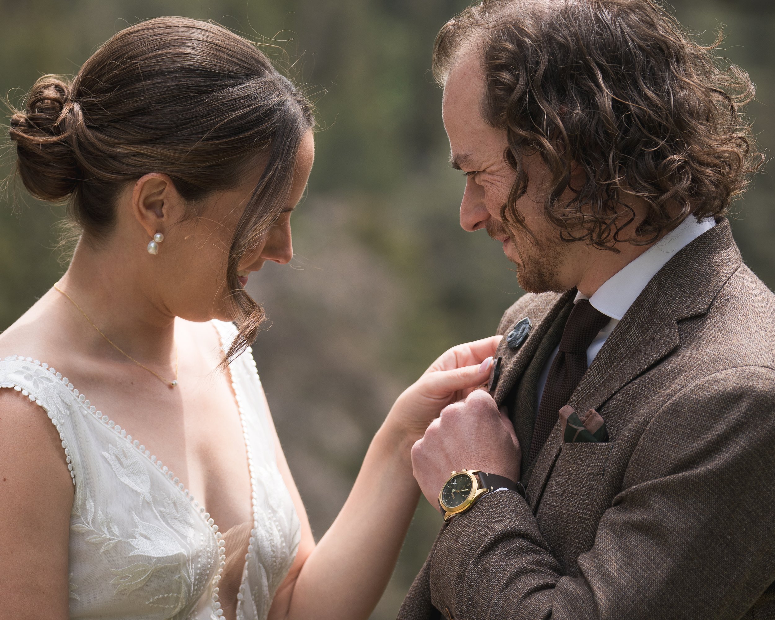 The bride observes a custom pet lapel pin on the groom, documentary wedding photography at Grand Targhee Resort