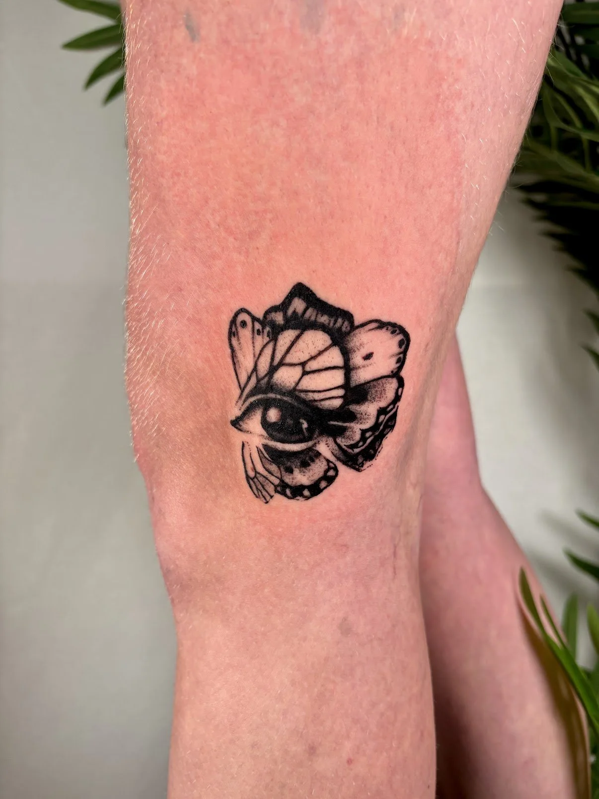 Black tattoo of a butterfly with a human eye on its body on a person's skin.