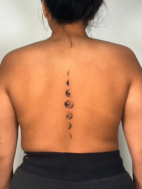 Back view of a woman with a moon phase tattoo running down the center of her back.