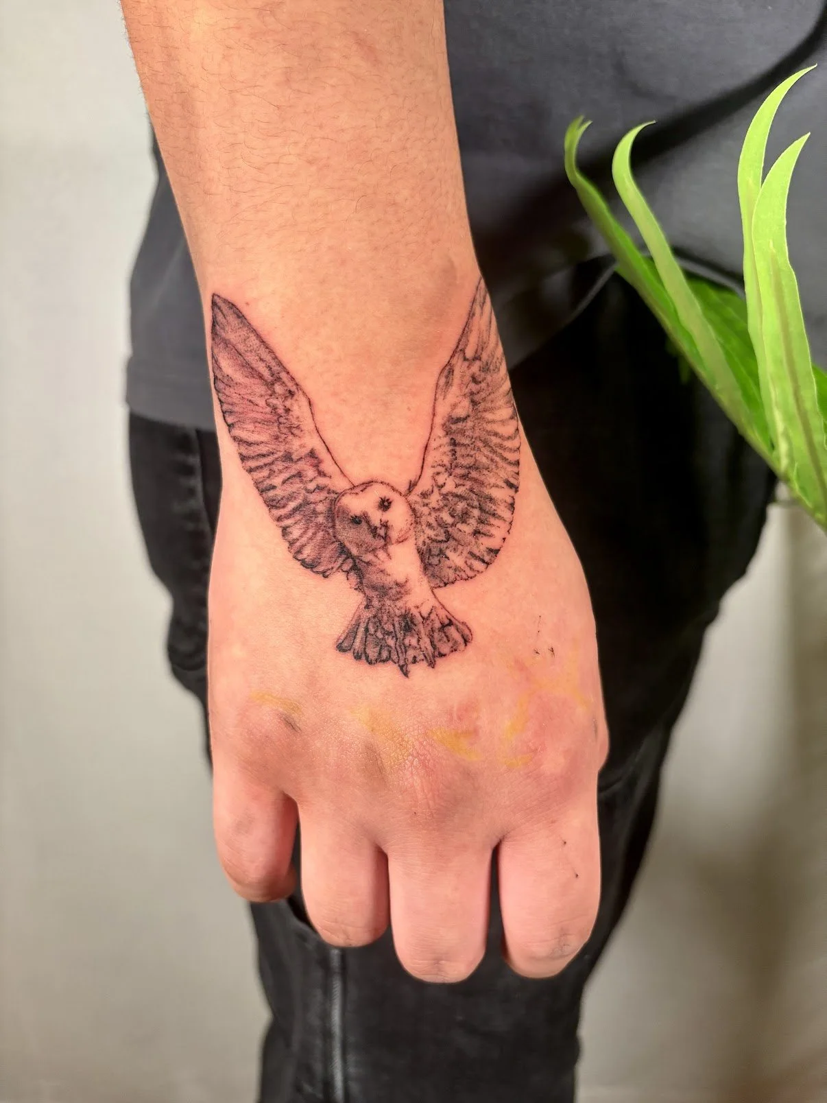 Black ink tattoo of a flying owl on a person's hand.
