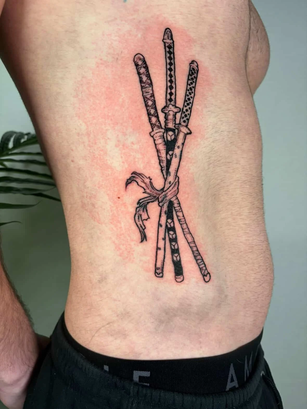 Tattoo of five swords tied together with a cloth on a person's side.