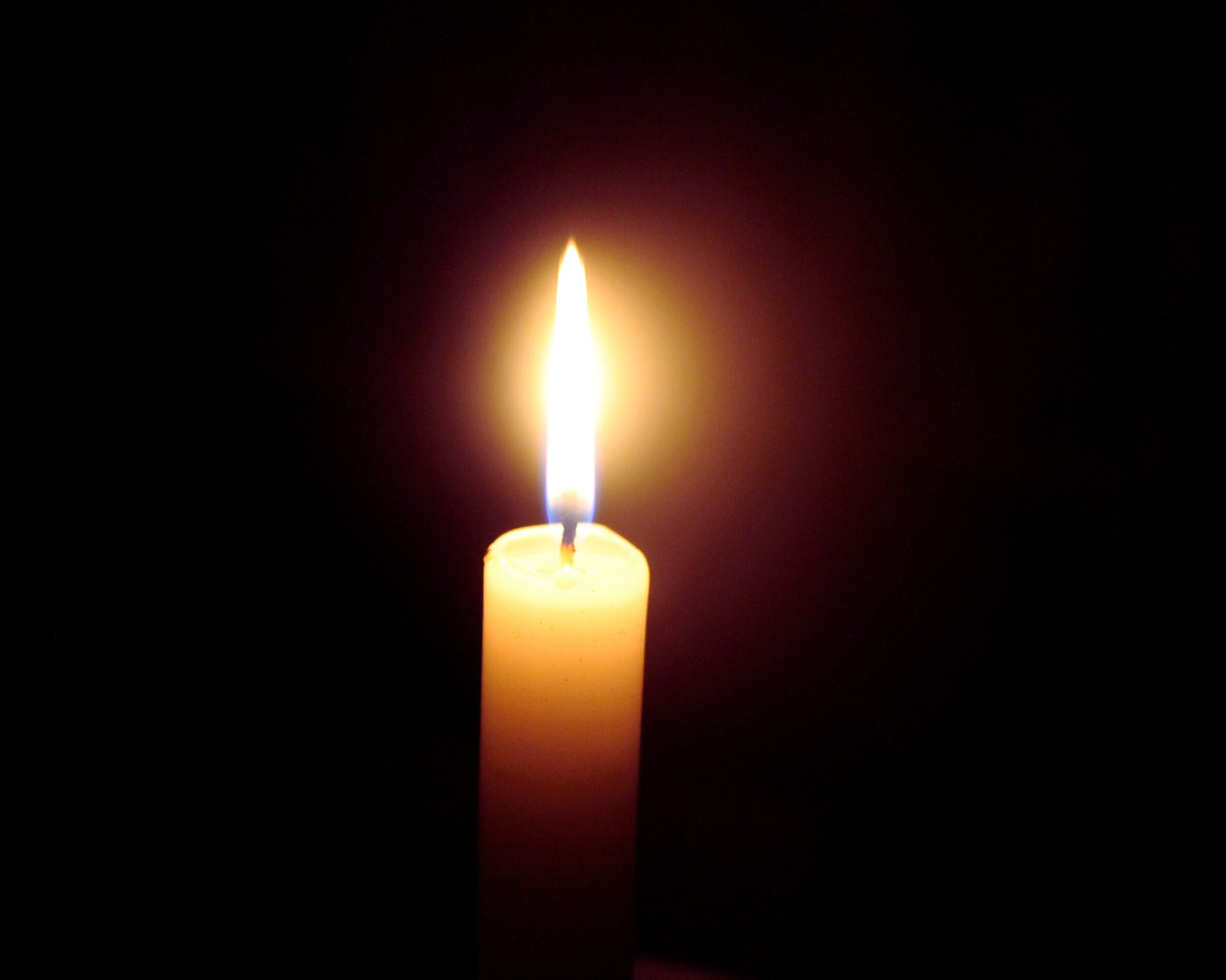 A lit yellow candle with a glowing flame in a dark background.
