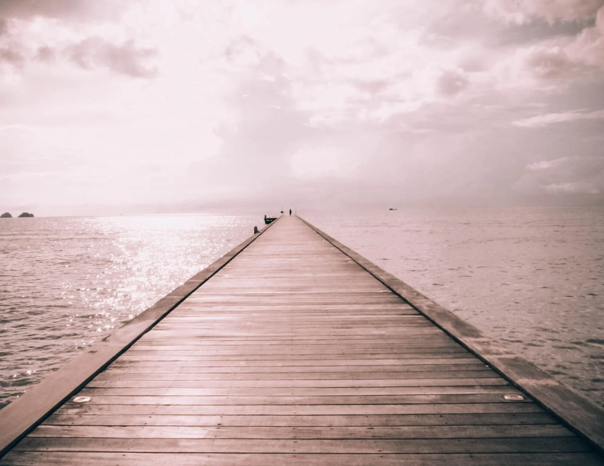 Wooden pier extending out over a calm body of water under a cloudy sky.