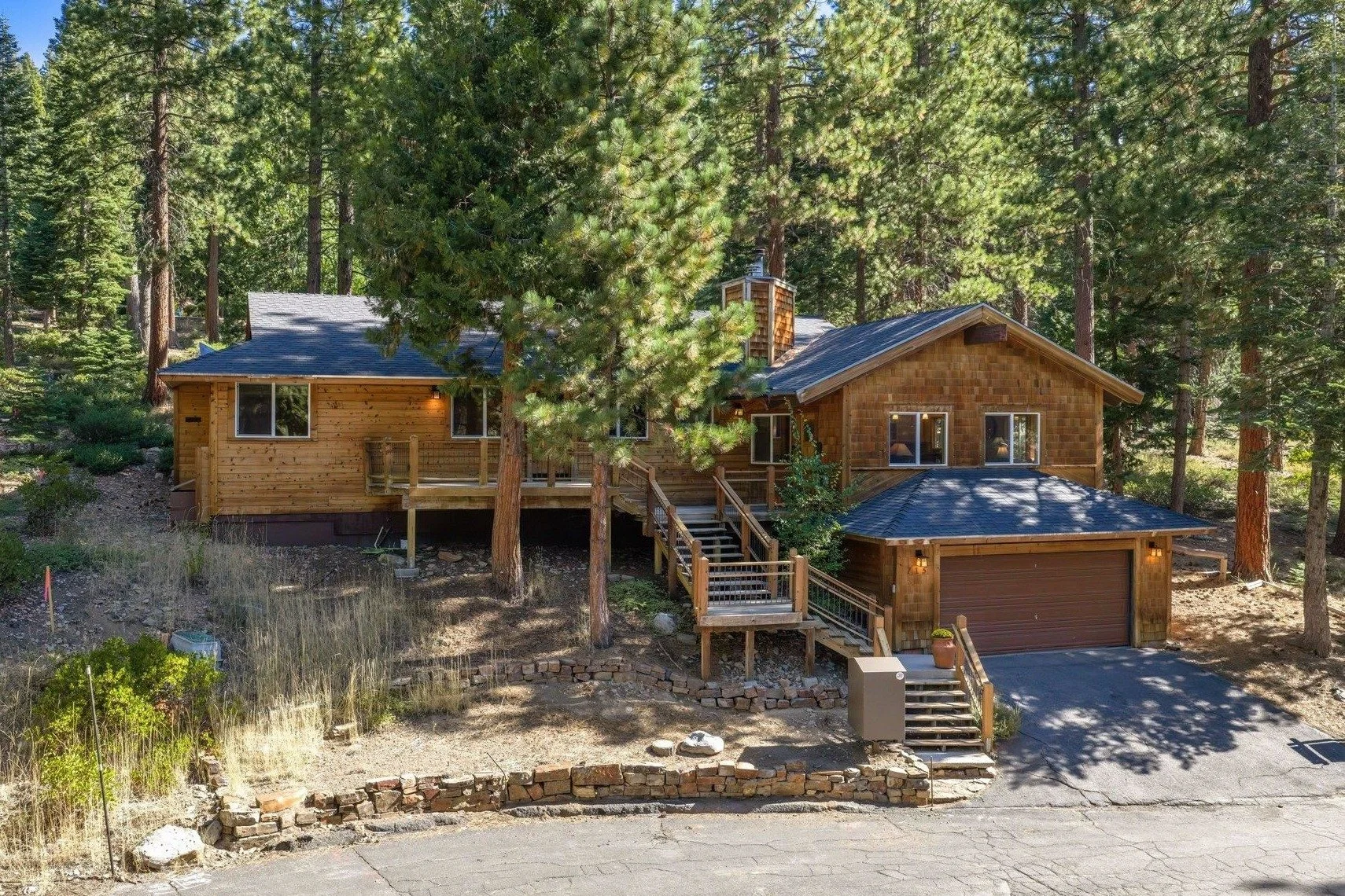 Wood-sided home at 715 Granite Road with a two-car garage, front deck and stairs among tall pines