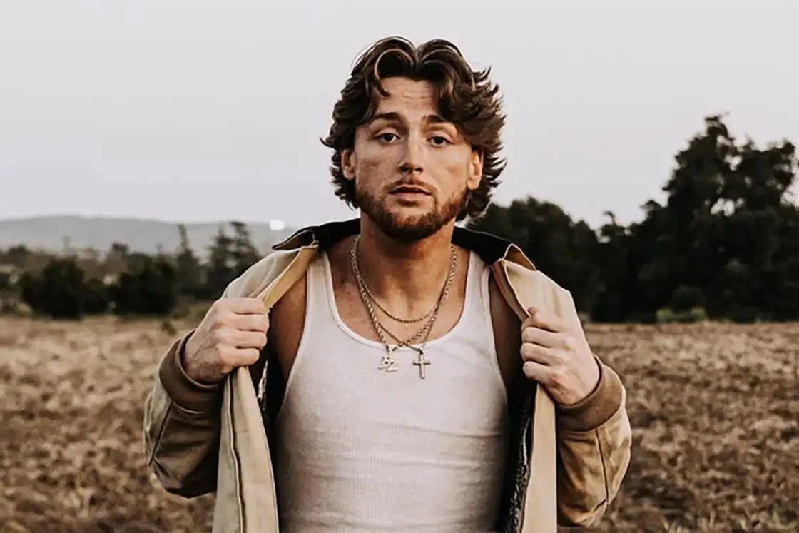 Bailey Zimmerman stands in a dry field wearing a light tank top and open tan jacket.
