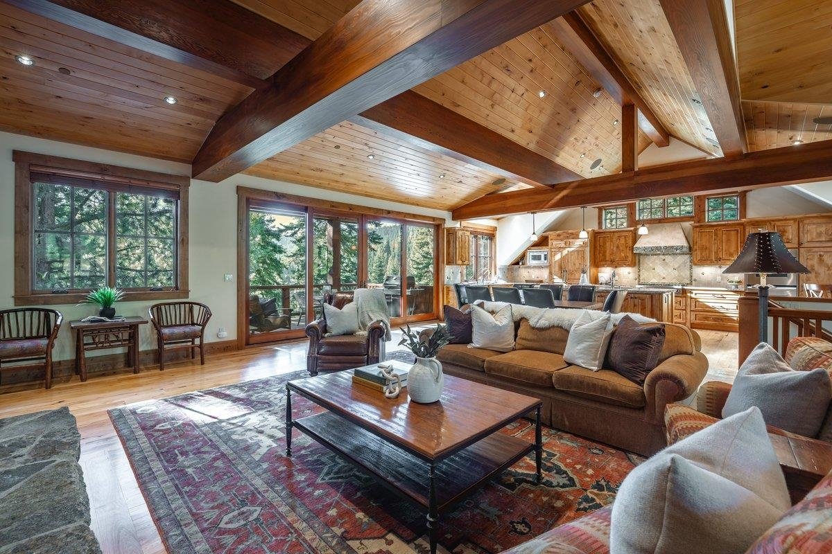 Open great room and kitchen at 1753 Grouse Ridge Road with exposed timber beams and forest-facing windows.